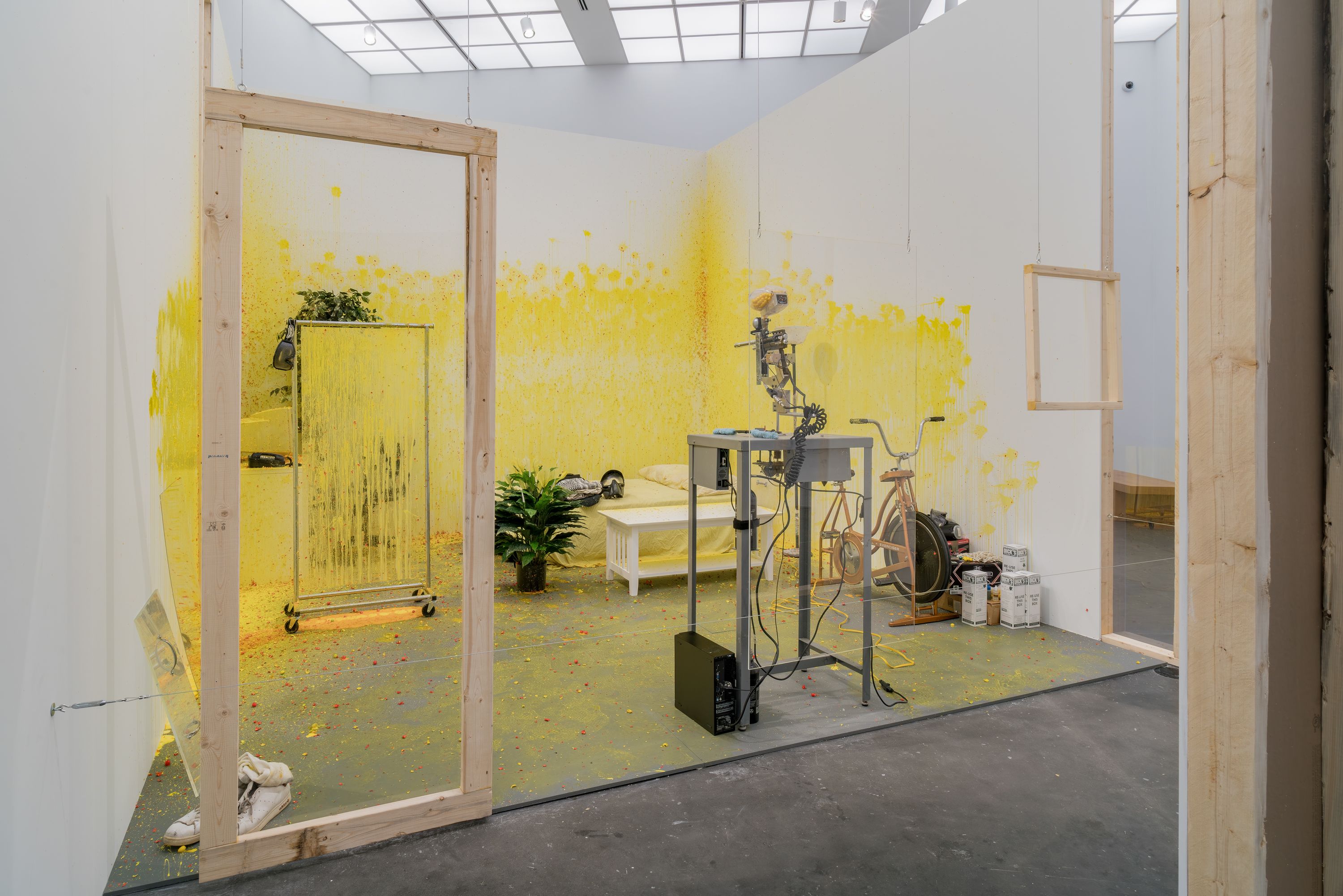 A plywood room with yellow paint on its wall installed in an art gallery