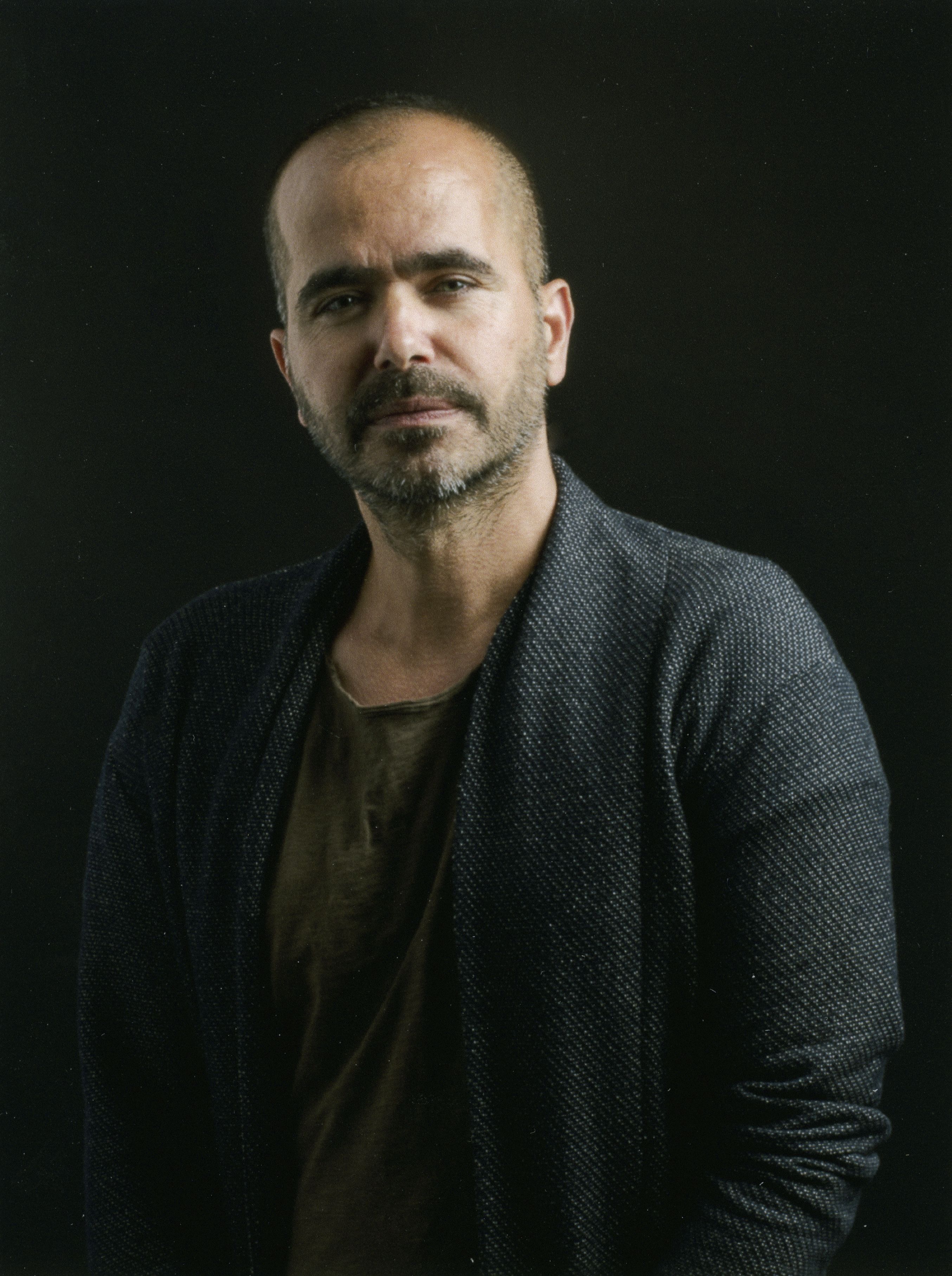 An artist in dark clothing stands in front of a black background