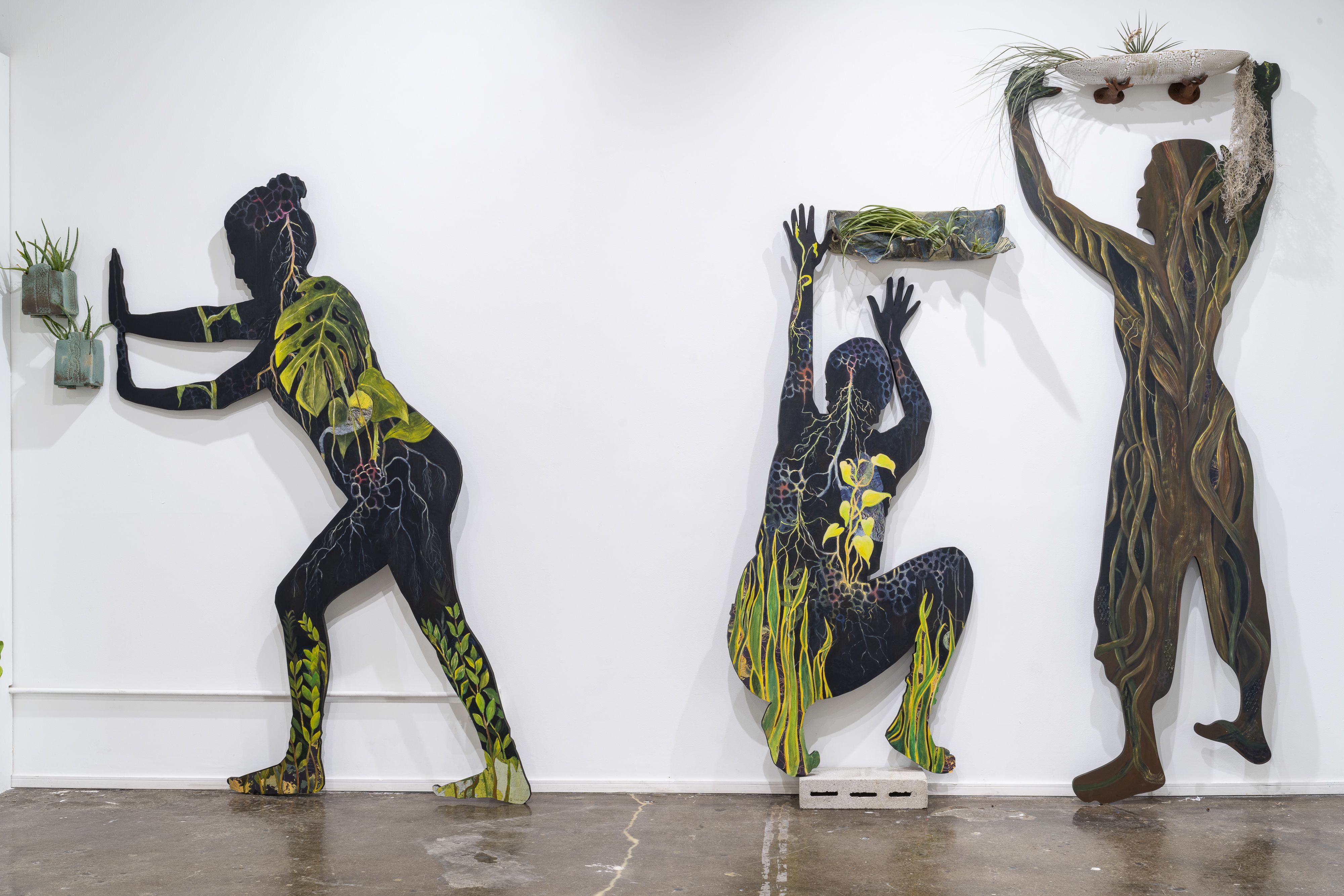 Three silhouetted figures painted with plants