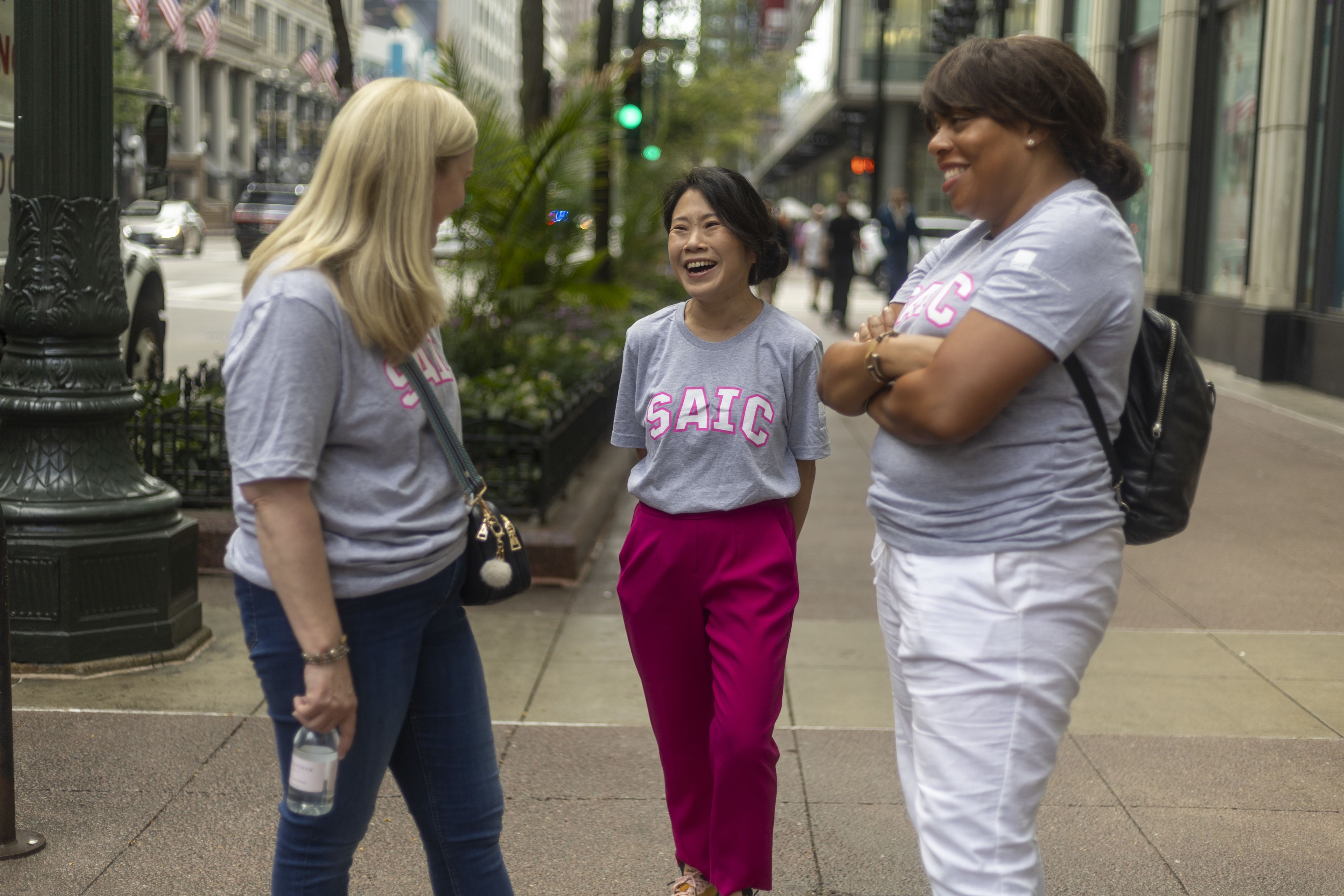 Three people stand on a city street in SAIC teeshirts