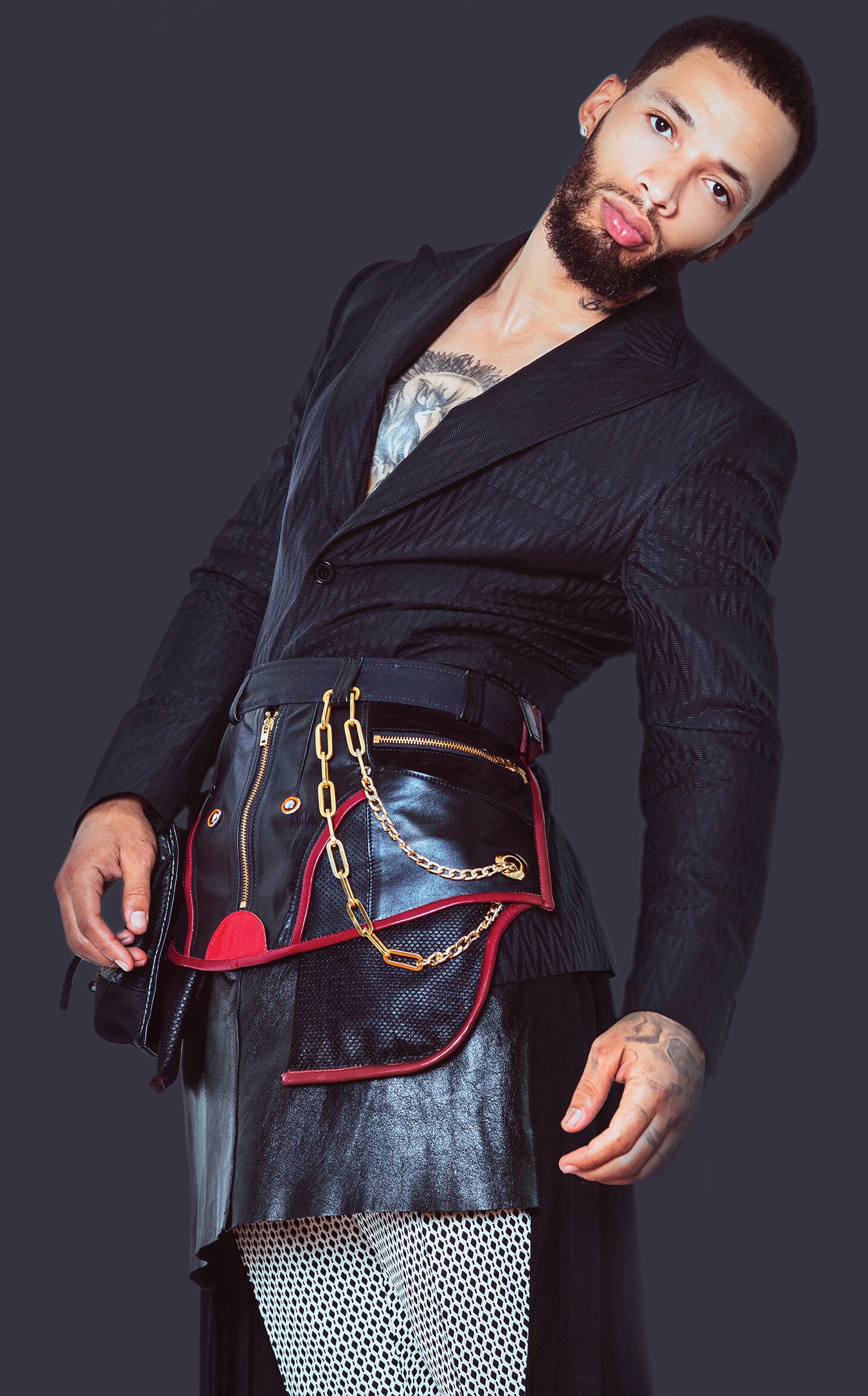 A model wears a black blazer with a leather skirt overlay laced with read thread and chains