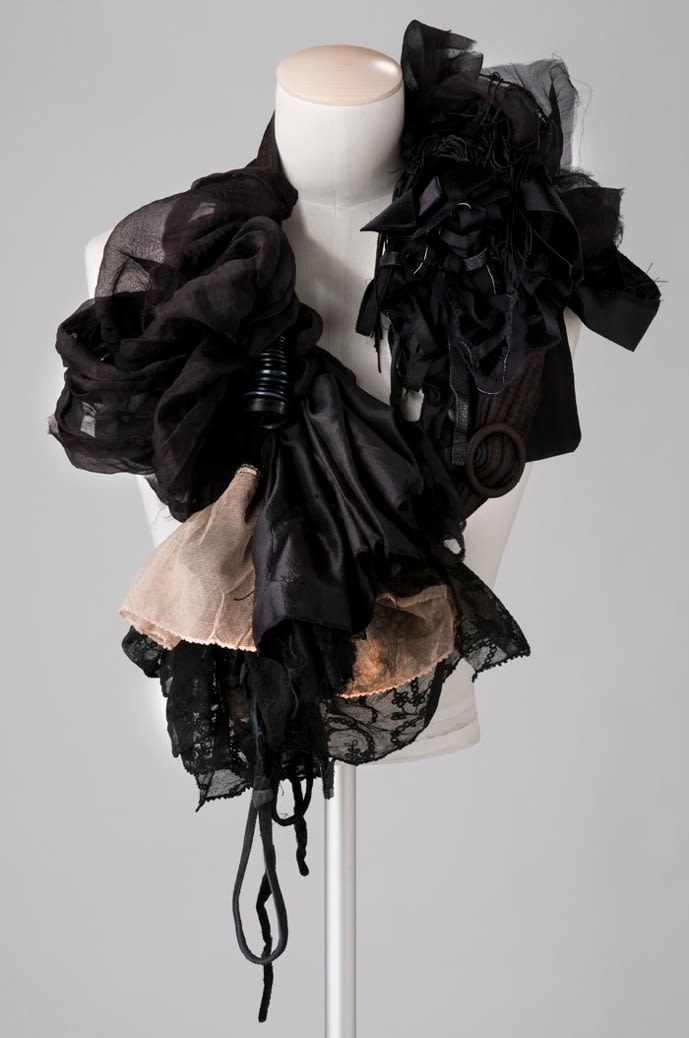 A white mannequin bust with pieces of black and nude silk fabric draped around the collar
