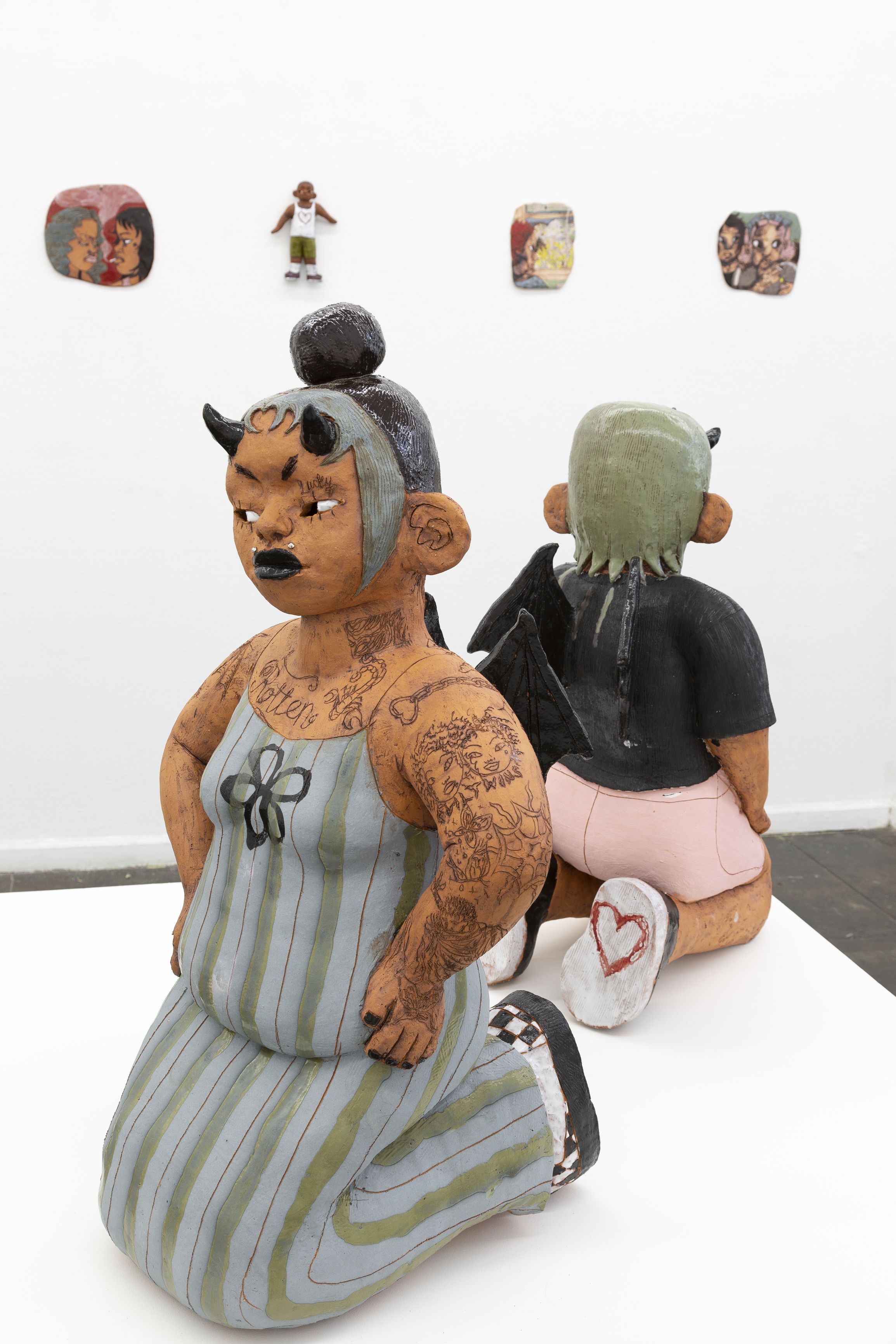 Ceramic woman with devil horns kneeling in a blue and green striped dress.