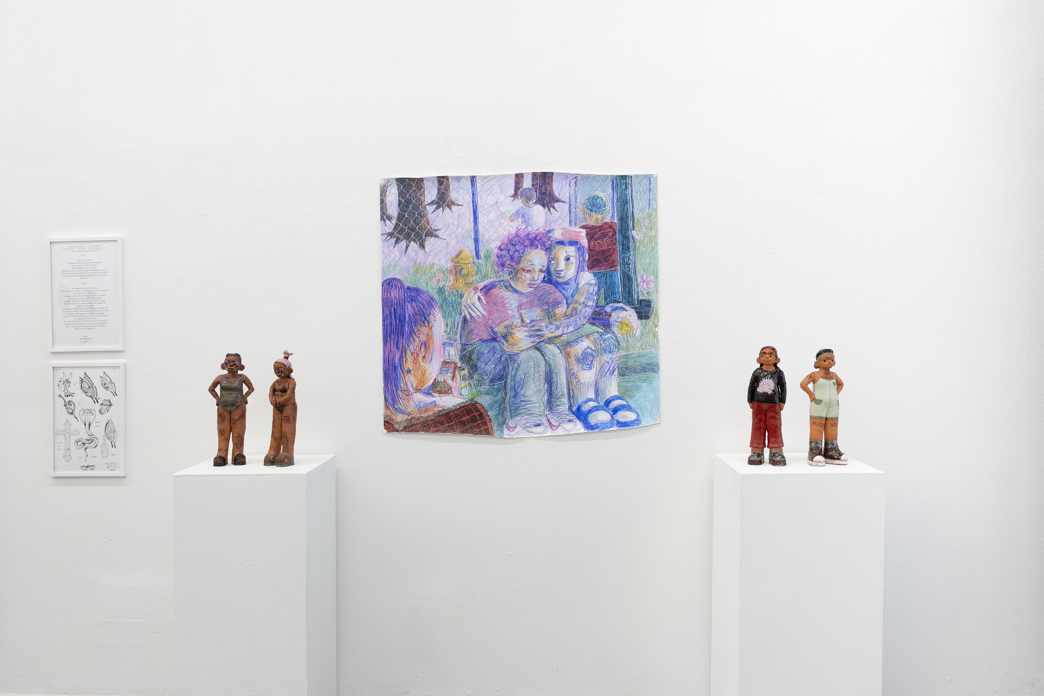 Small ceramic figures on two pedestal on either side of a small drawing of two people hugging.