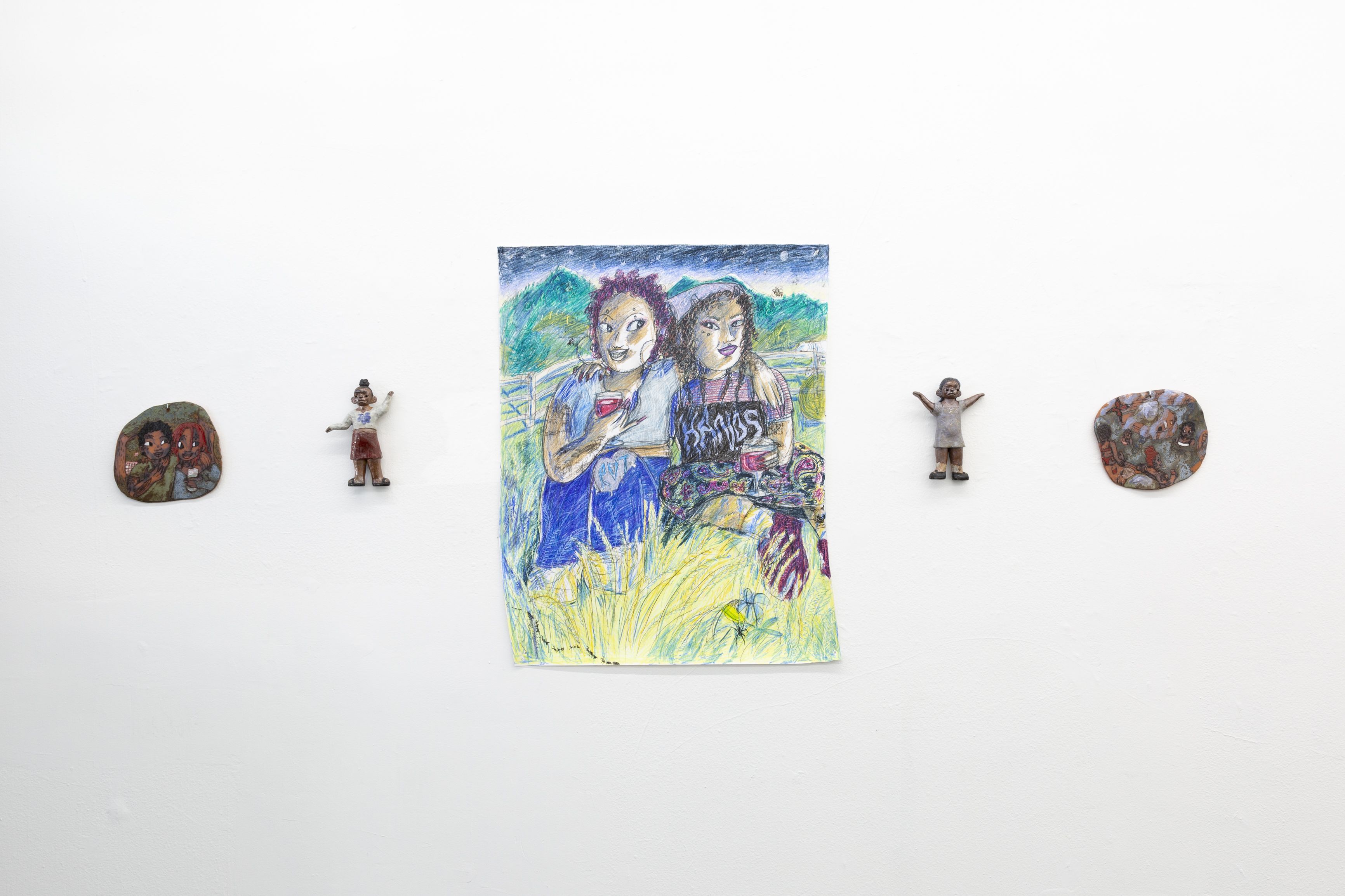 Two small ceramic figures and two small discs on either side of a small drawing of two people sitting in a field.