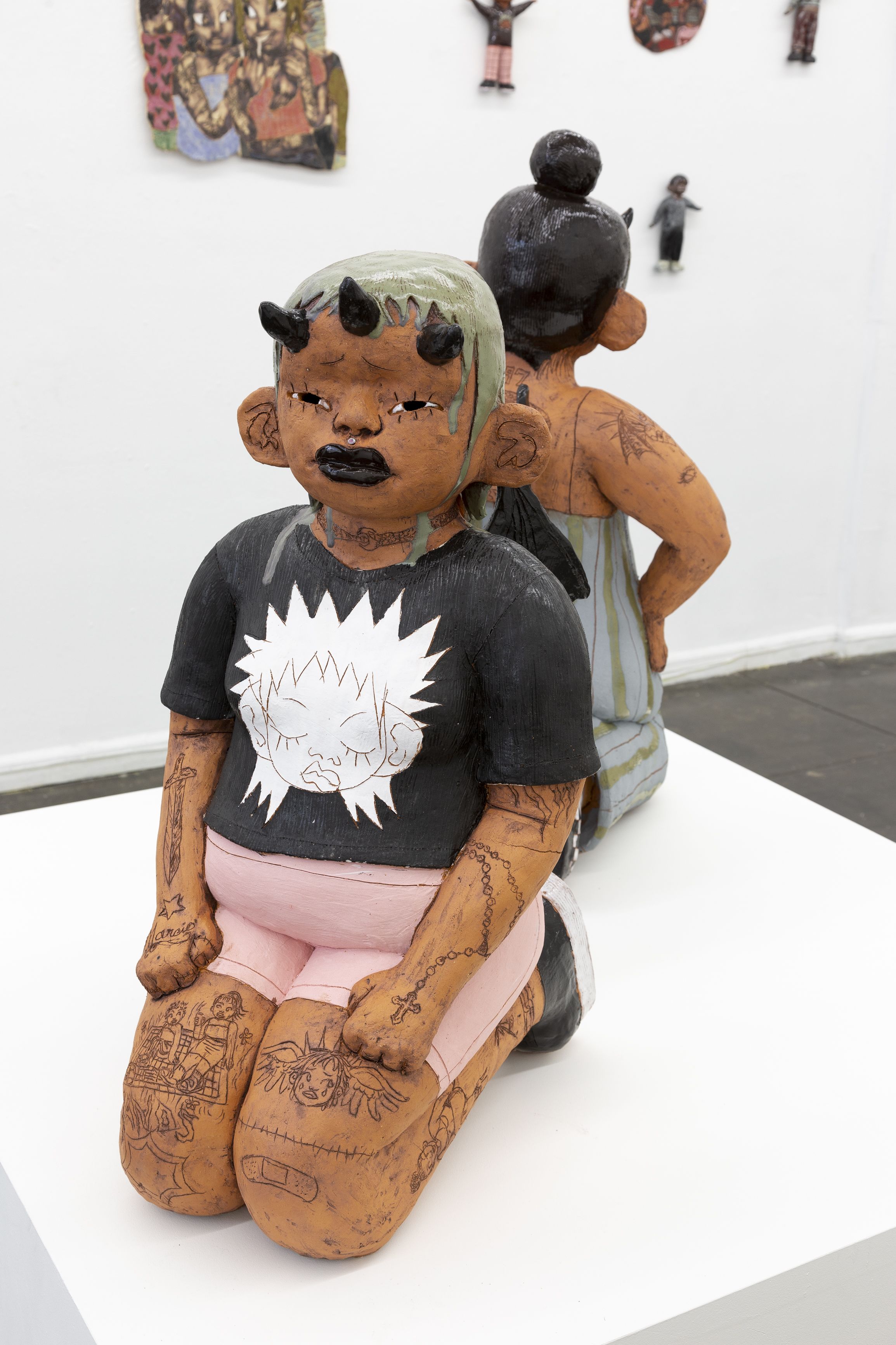 Ceramic woman with 3 devil horns kneeling in a black t-shirt with light pink shorts.