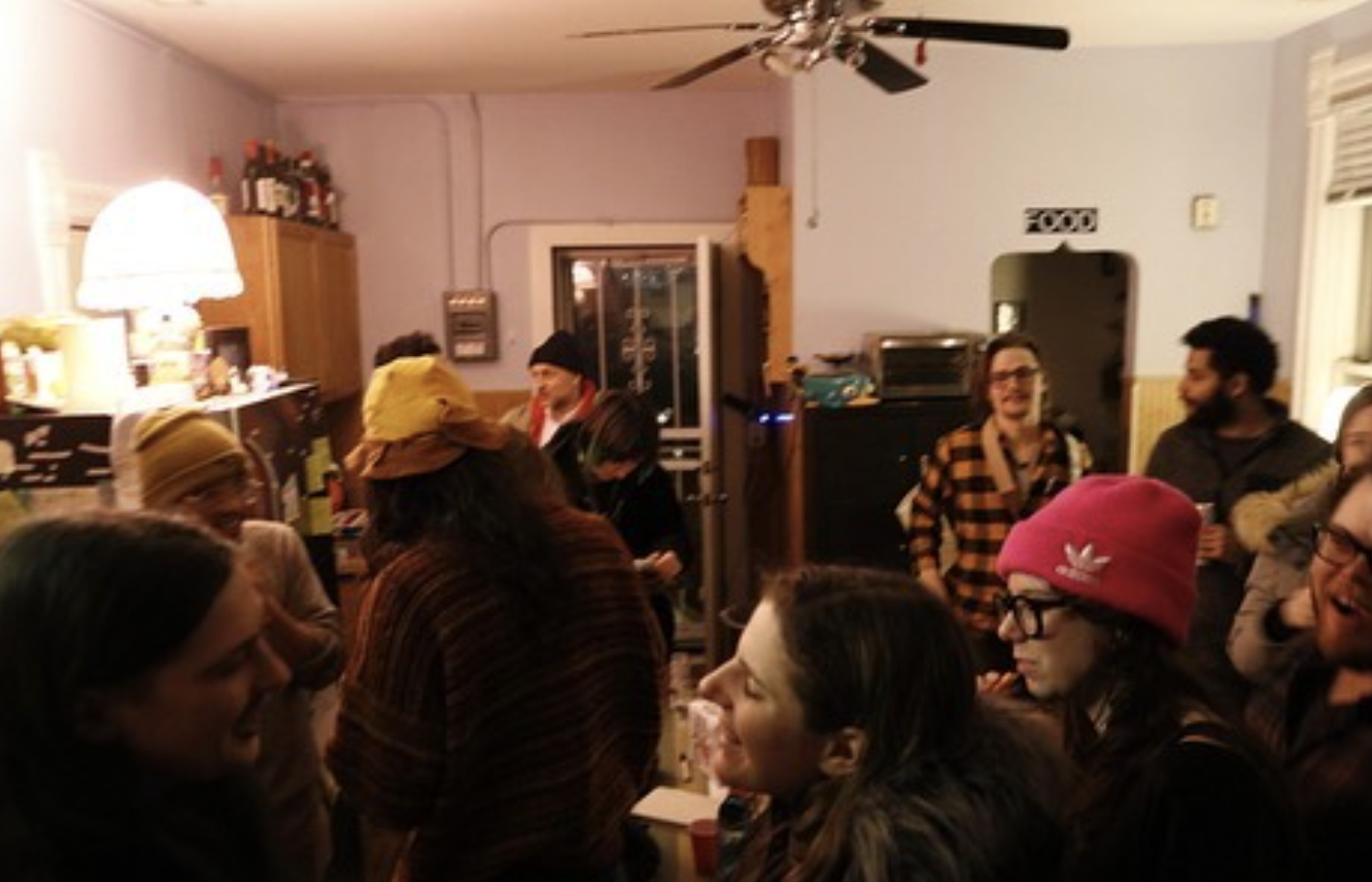 A group of people stand in a furnished room and talk to each other.