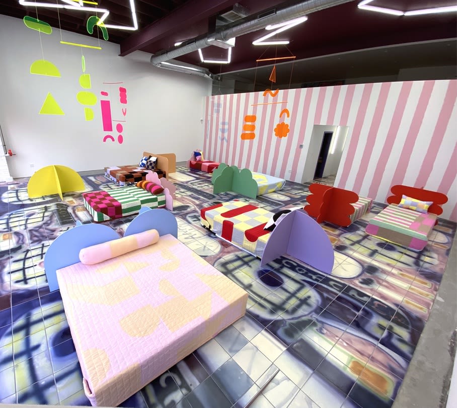 A room with a graphic print rug, brightly colored furniture, and neon mobiles 