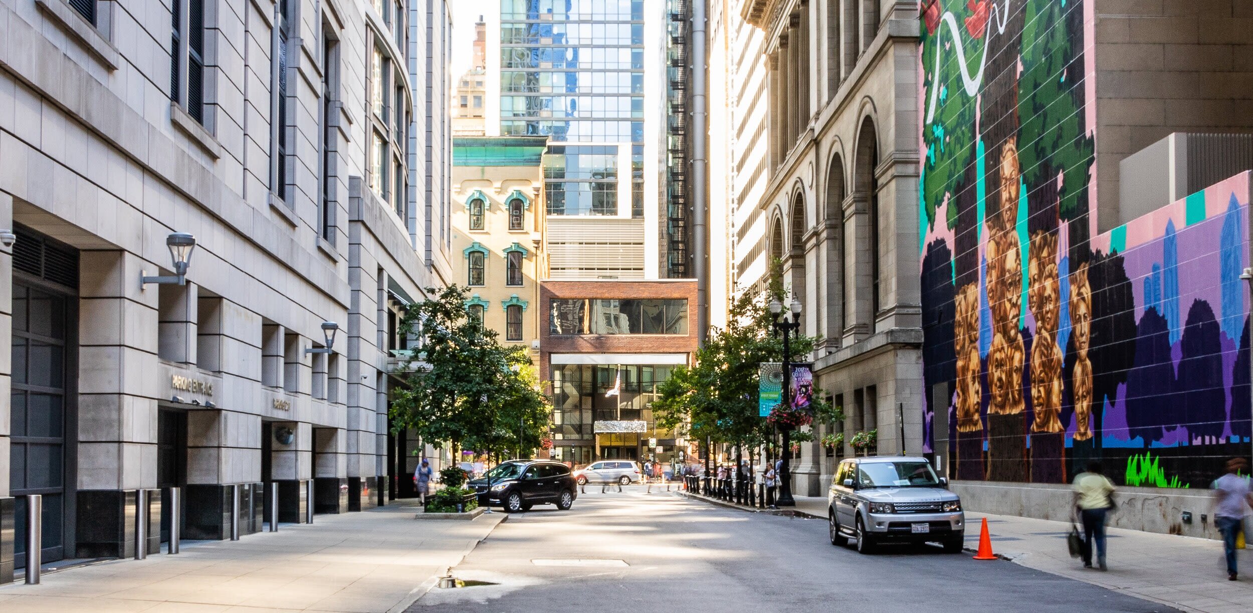 A street in Chicago's downtown, with a vibrant mural depicting women's faces and trees on the right