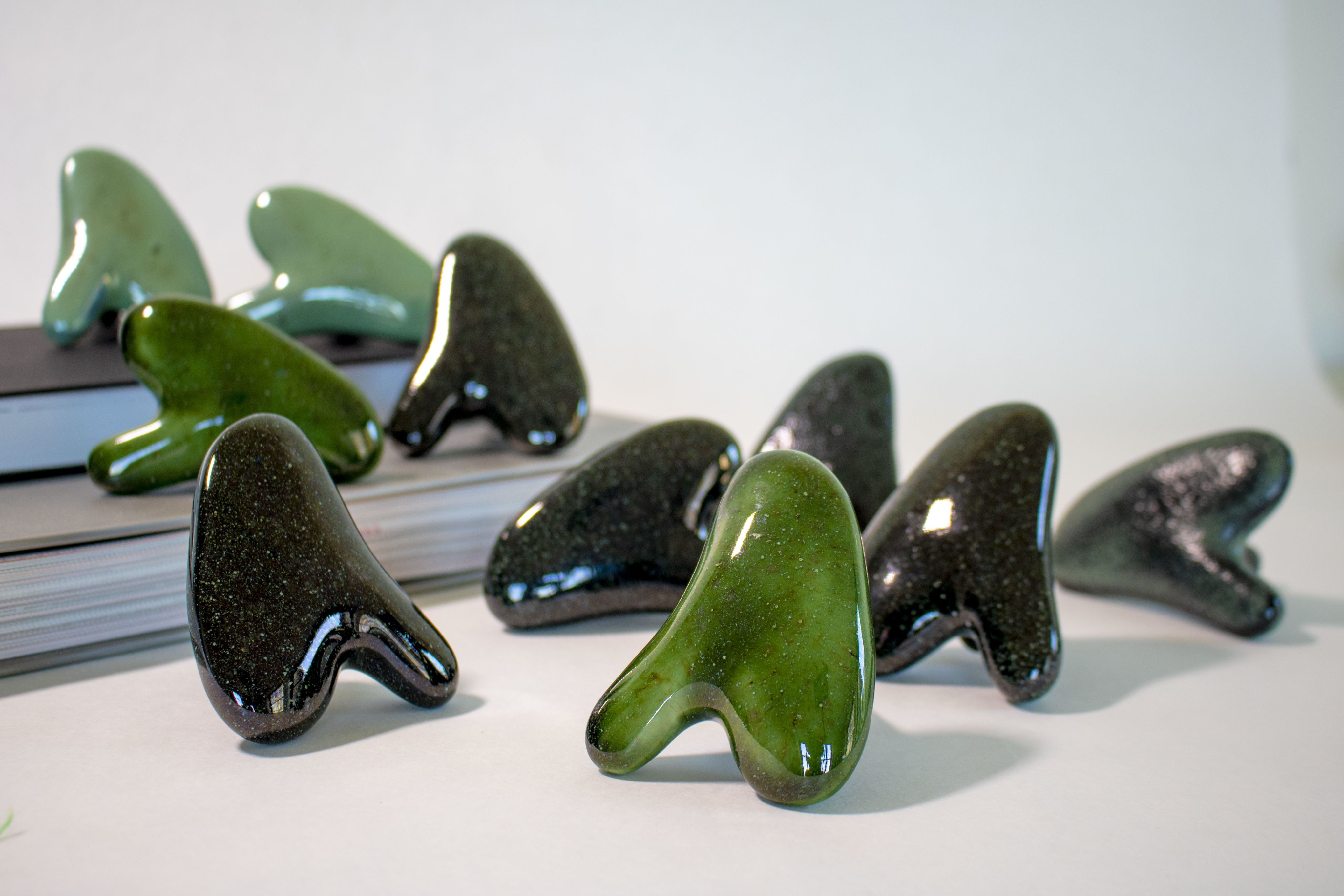 Green and black rounded triangular knobs made of high-fired porcelain sit in front of a pile of books. Some of them are placed on top of the pile of books