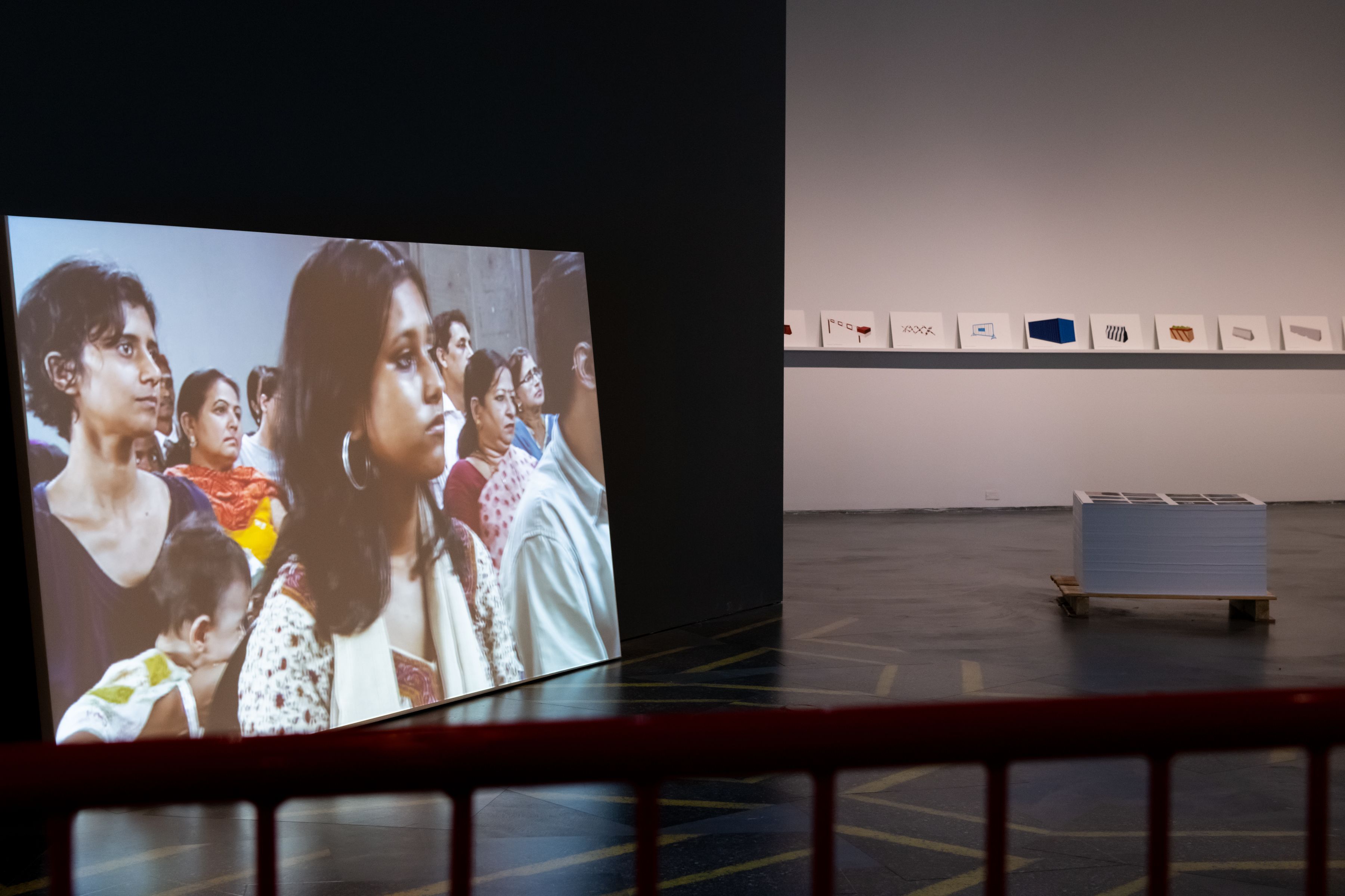 A gallery photo showing both a still from a film of several woman projected on a large screen and a sequence of prints lined up on a nearby wall