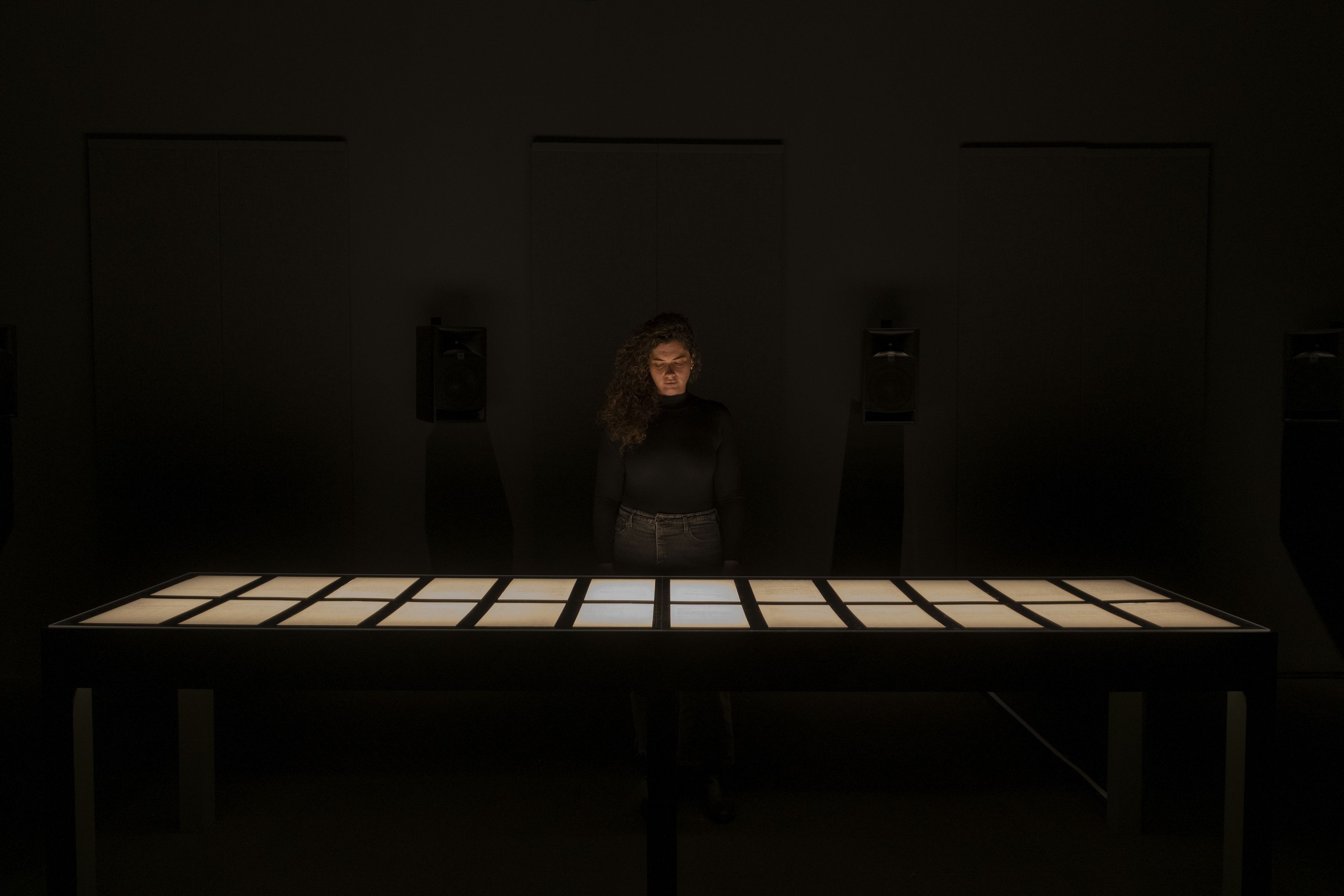 A woman in a dark room stands in front of a projected grid of light on a surface