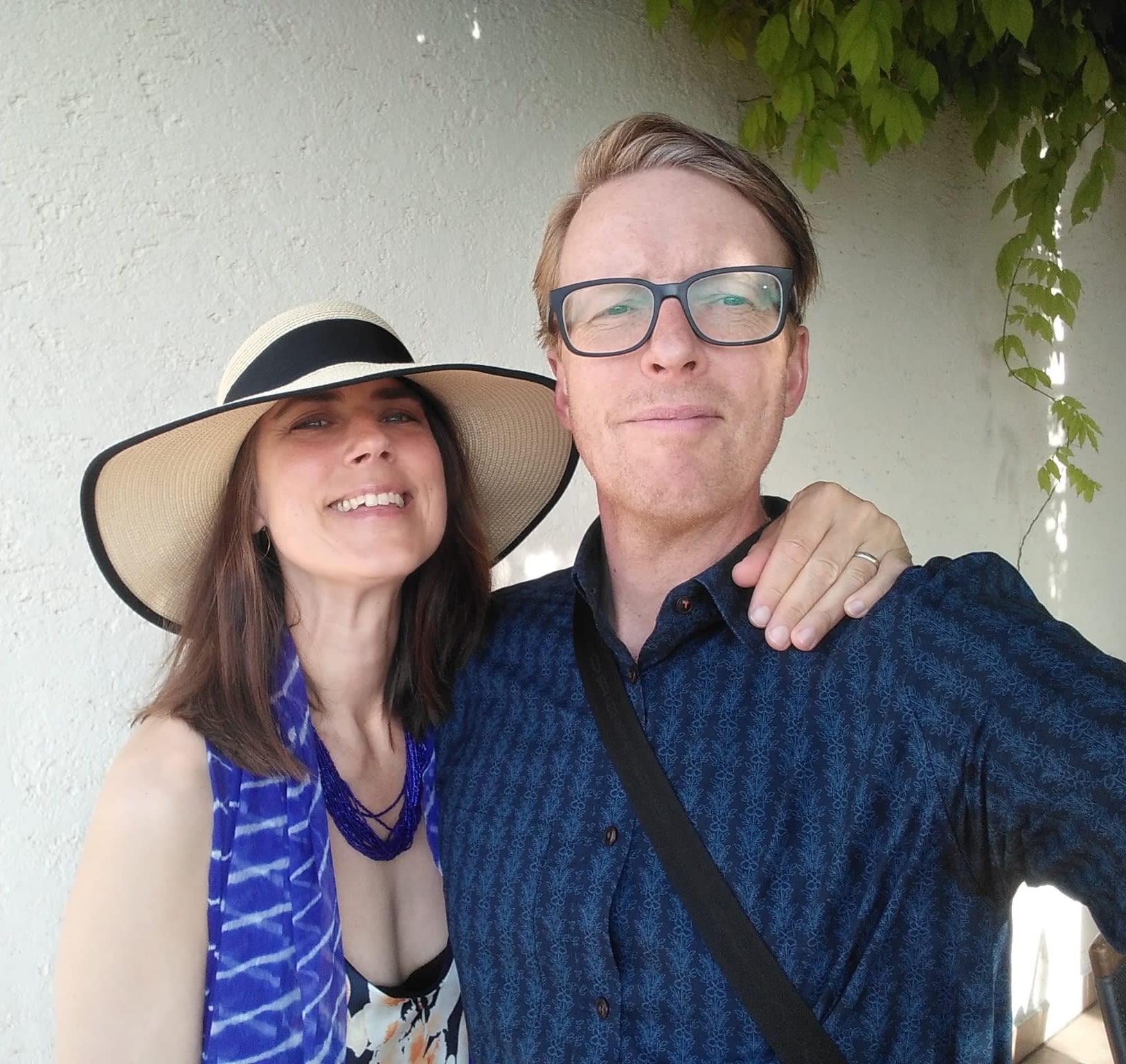 A couple pose for a photo in front of a white wall and vines