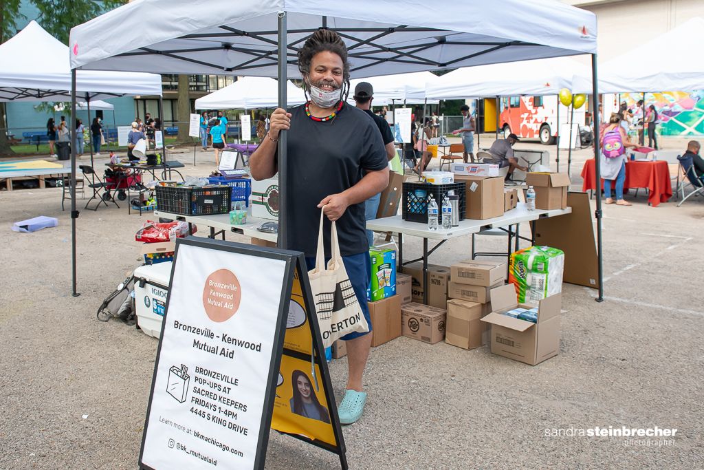 A man stands in a parking lot in front of a stand at an outdoor market