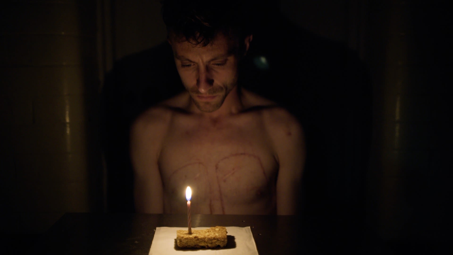 An artist sits in a dark room lit by a candle on a cake