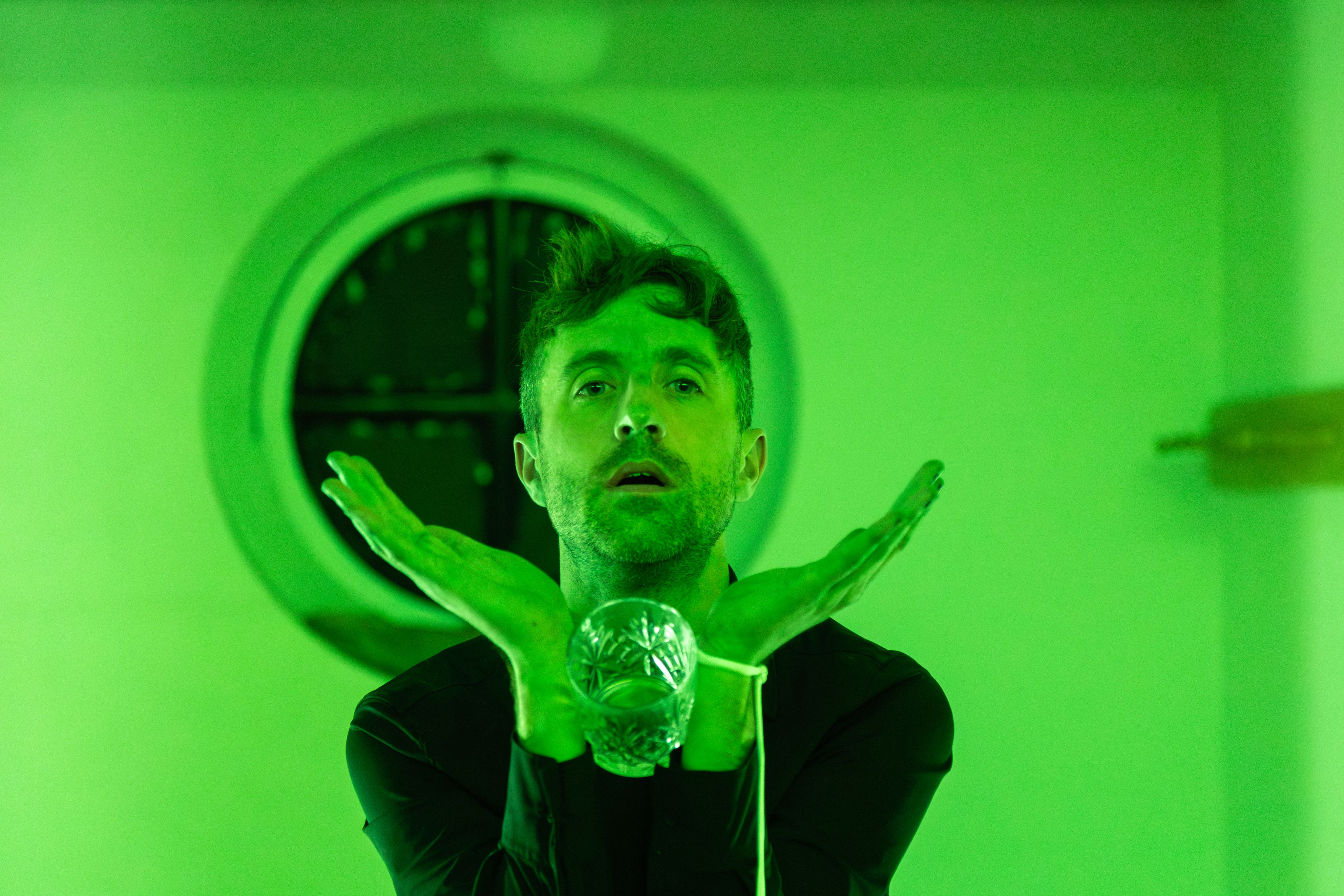 A green-tinged portrait of an artist holding a glass