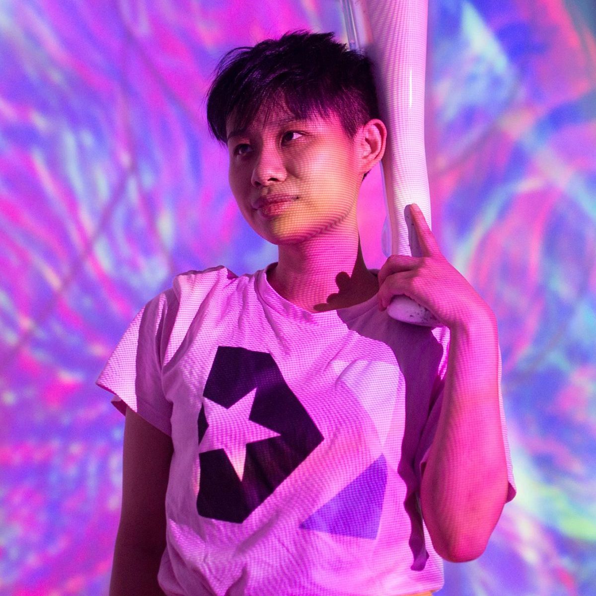 A photo of a young woman in a t-shirt with a star on it standing in a modern art space lit by pink and purple projections
