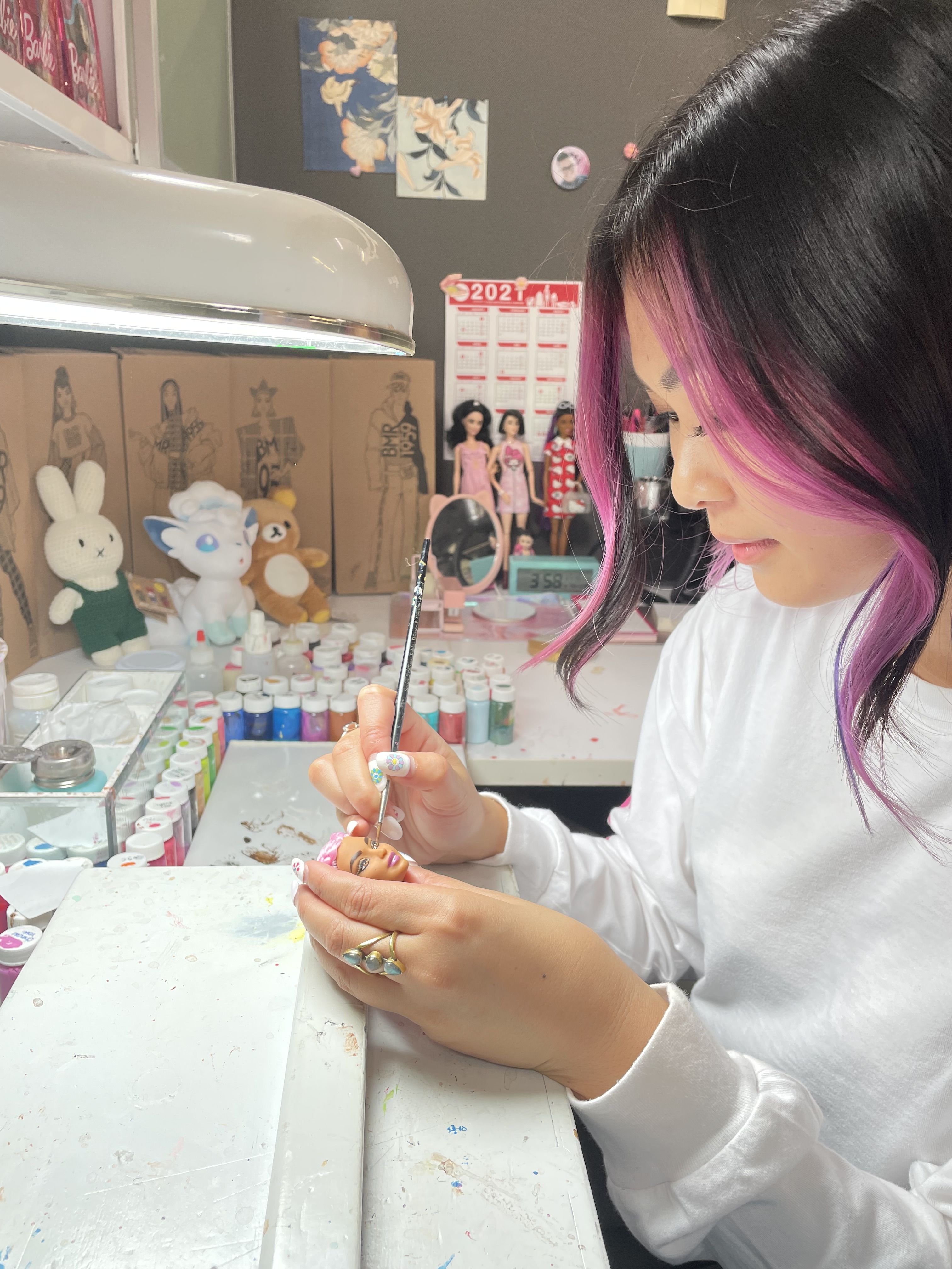 An artist sits at her desk painting a doll head