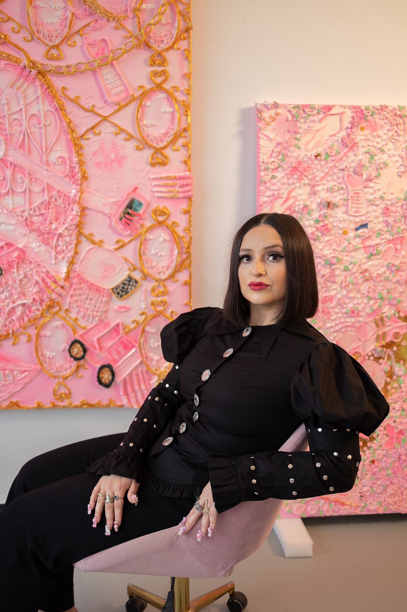 An artist sits in front of two of her pink canvases 