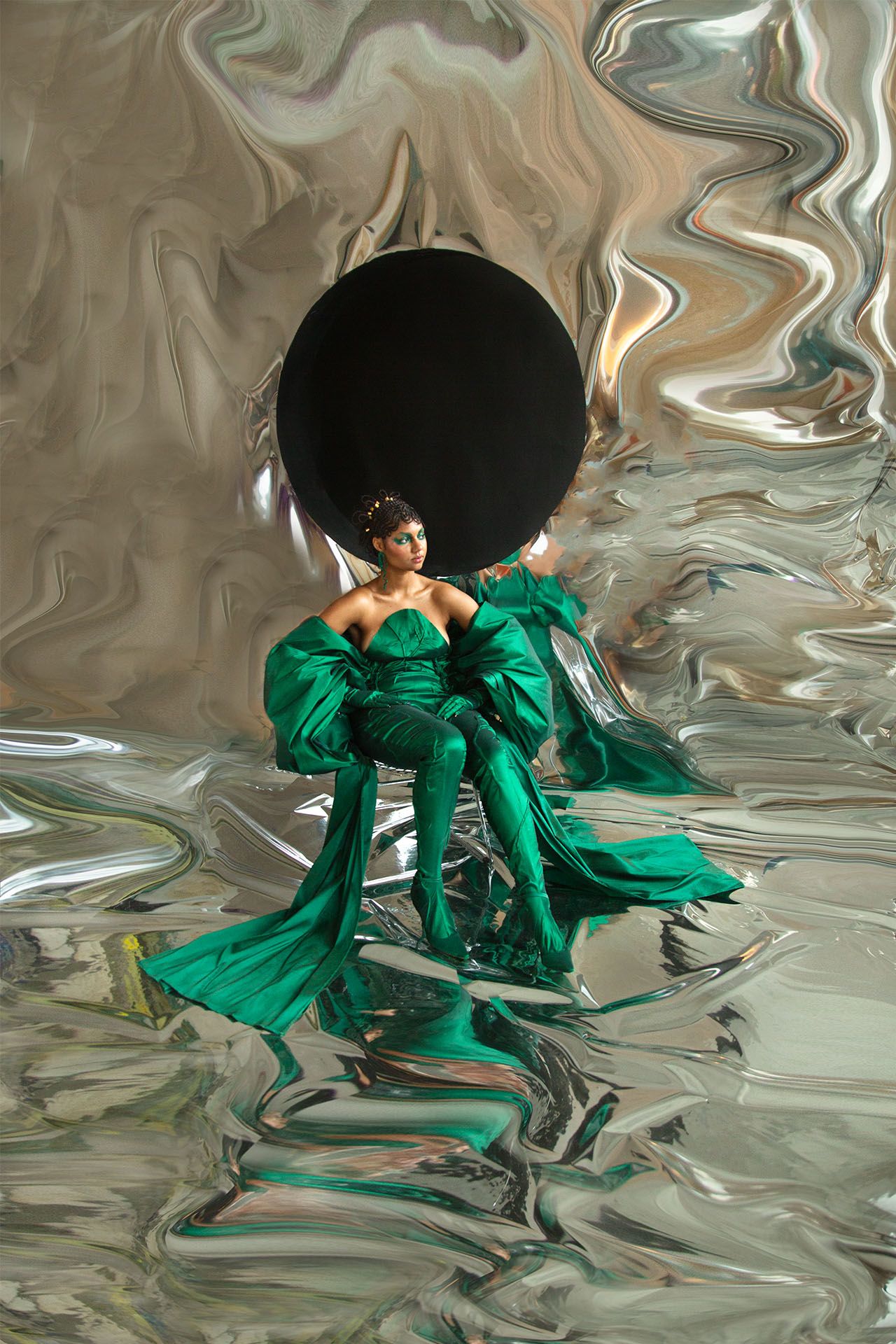 A model in a green jumpsuit with voluminous sleeves poses in front of a silver backdrop