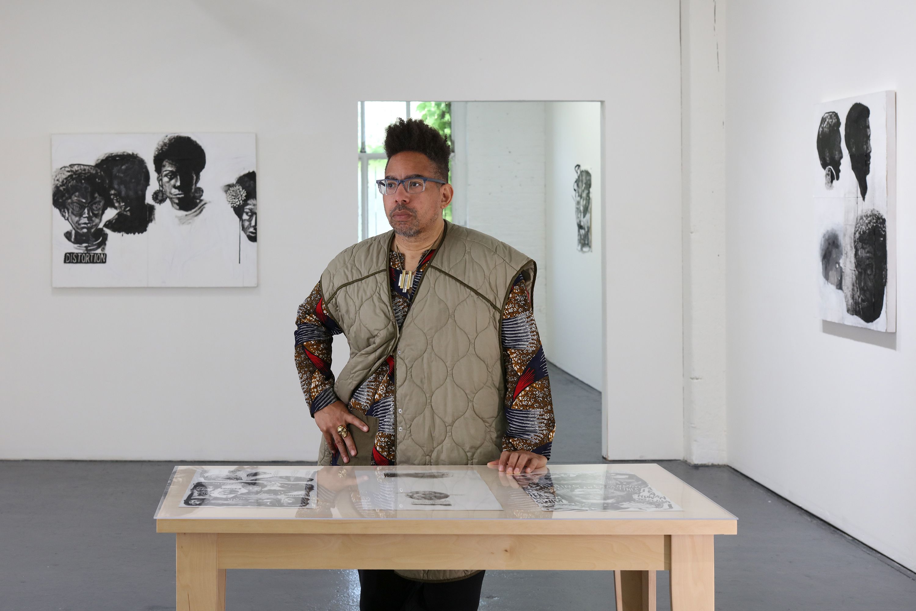 An artist in a quilted vest stands in a modern gallery space