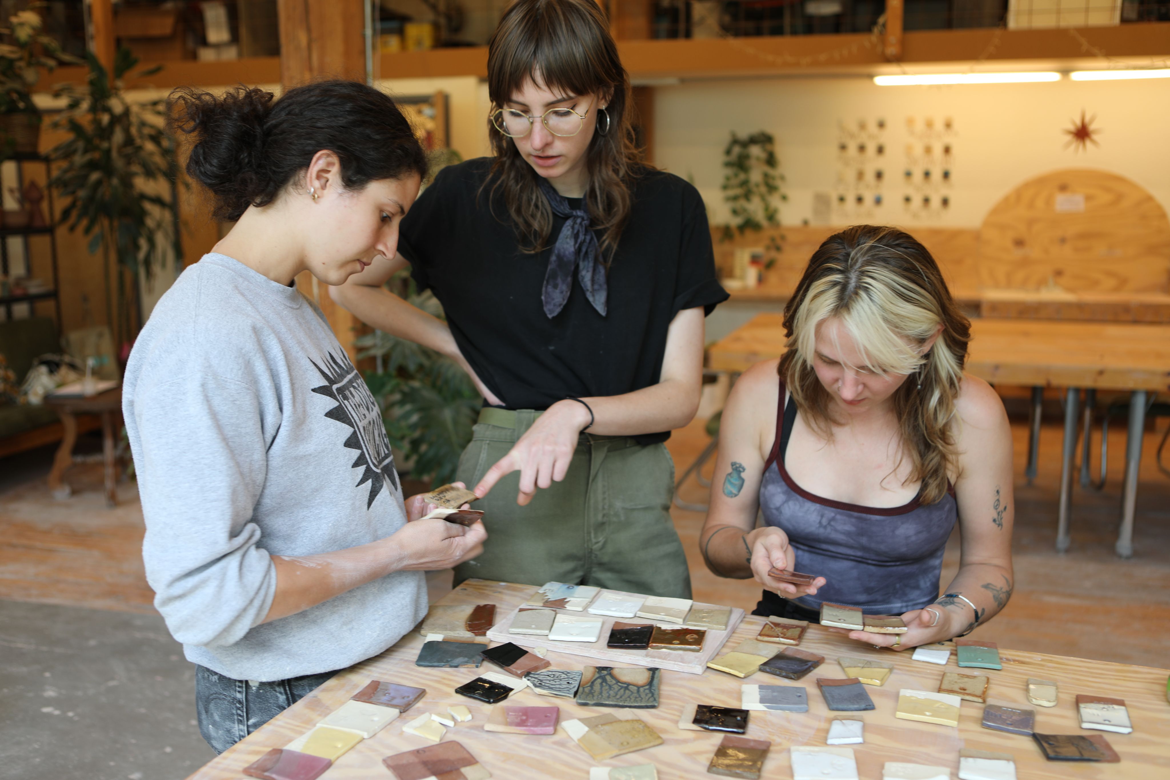 Three artists look at glaze tiles on a table