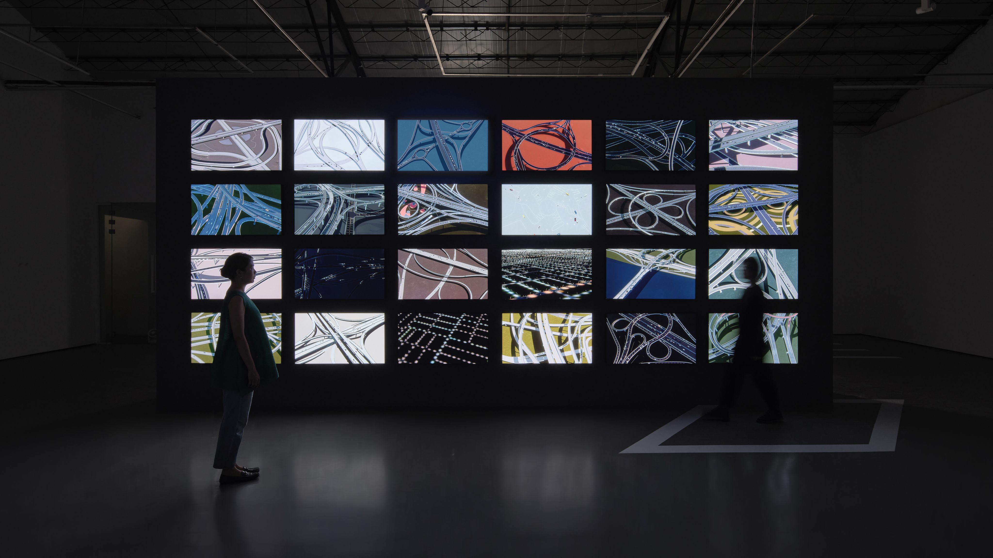 A figure stands in front of a bank of screens in a dark room