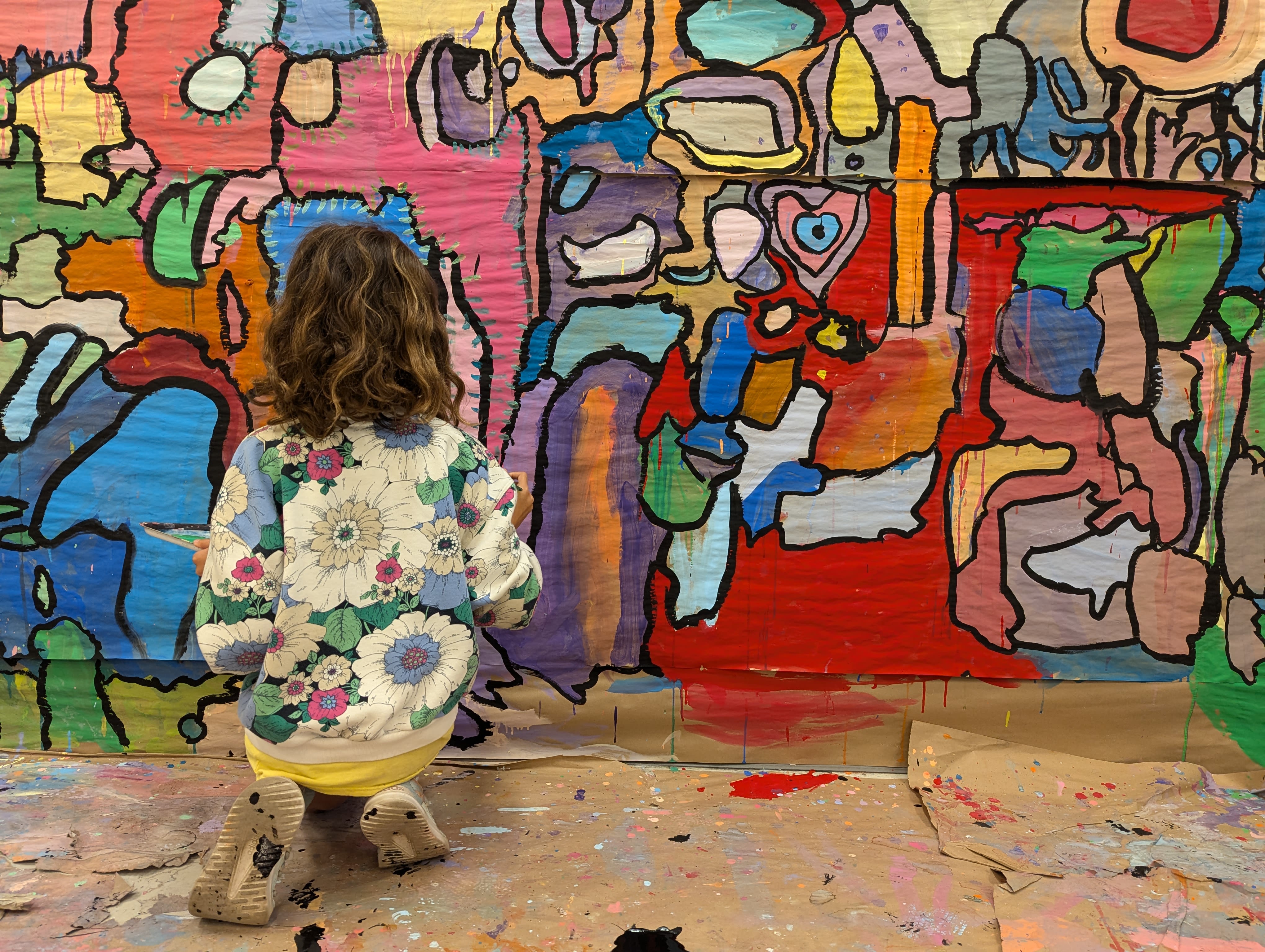A student kneels to work on a colorful mural
