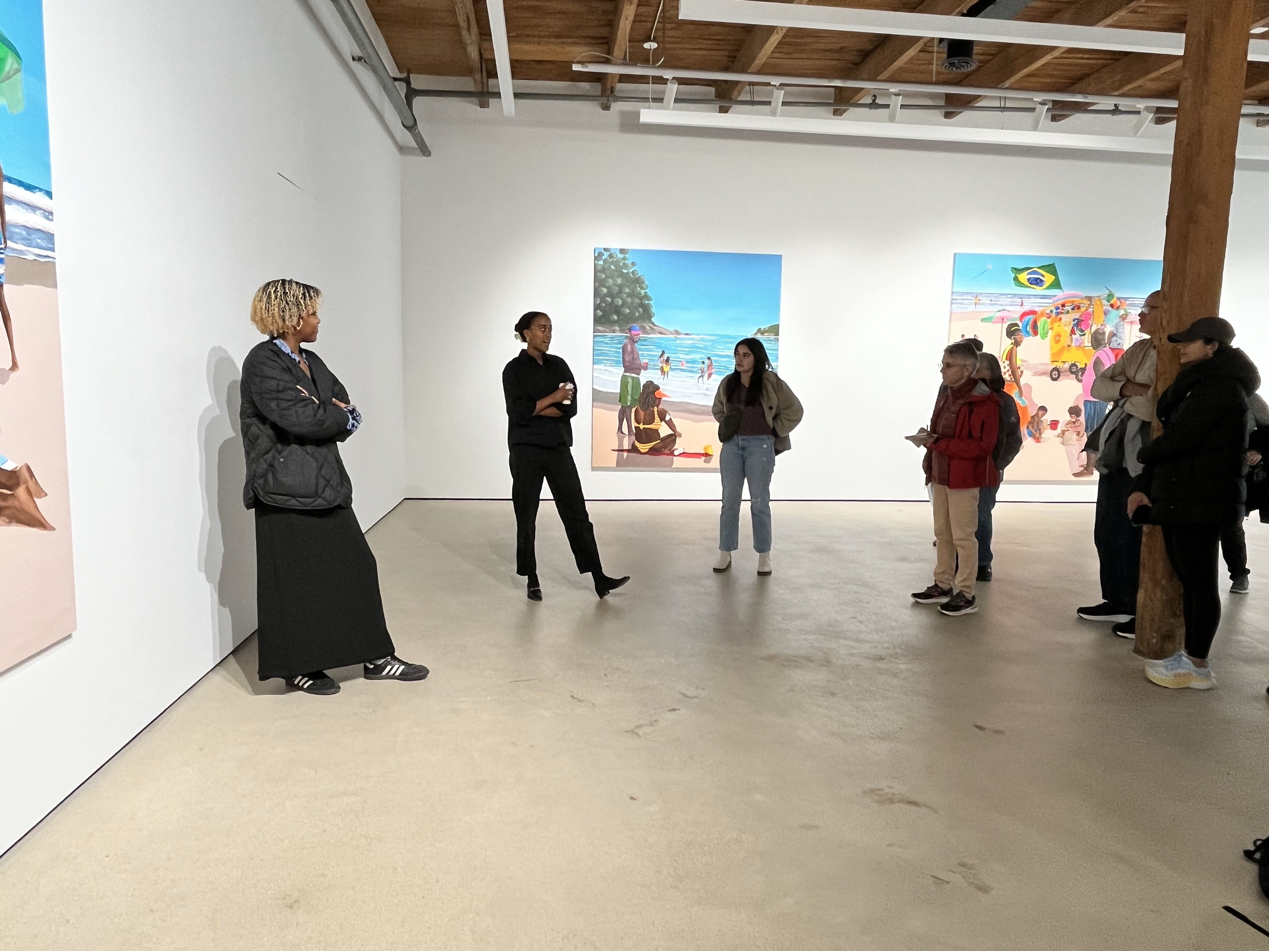 A group of people stand in a gallery in front of several large paintings