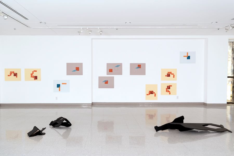 A gallery with black sculptures on the floor and abstract drawings pinned to a white wall