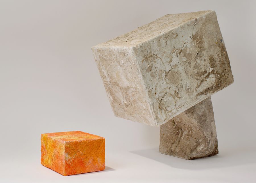 Two square sculptures—one orange and one gray and white—posed on a white backdrop