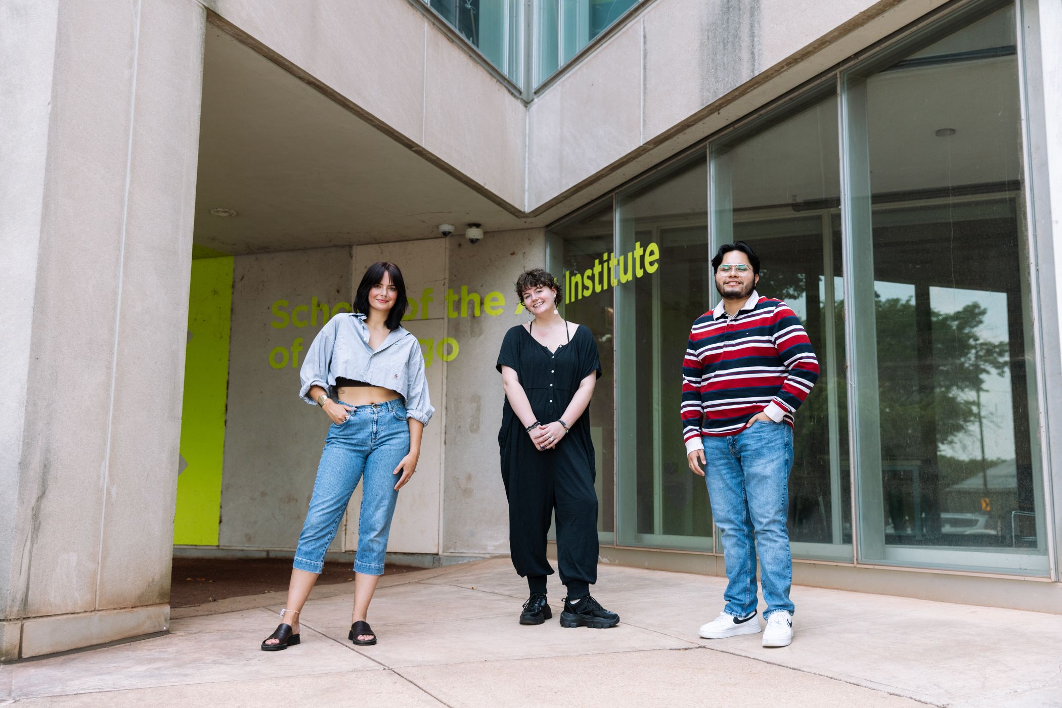 Three students stand outside a modern concrete building with School of the Art Institute of Chicago etched on the wall and glass