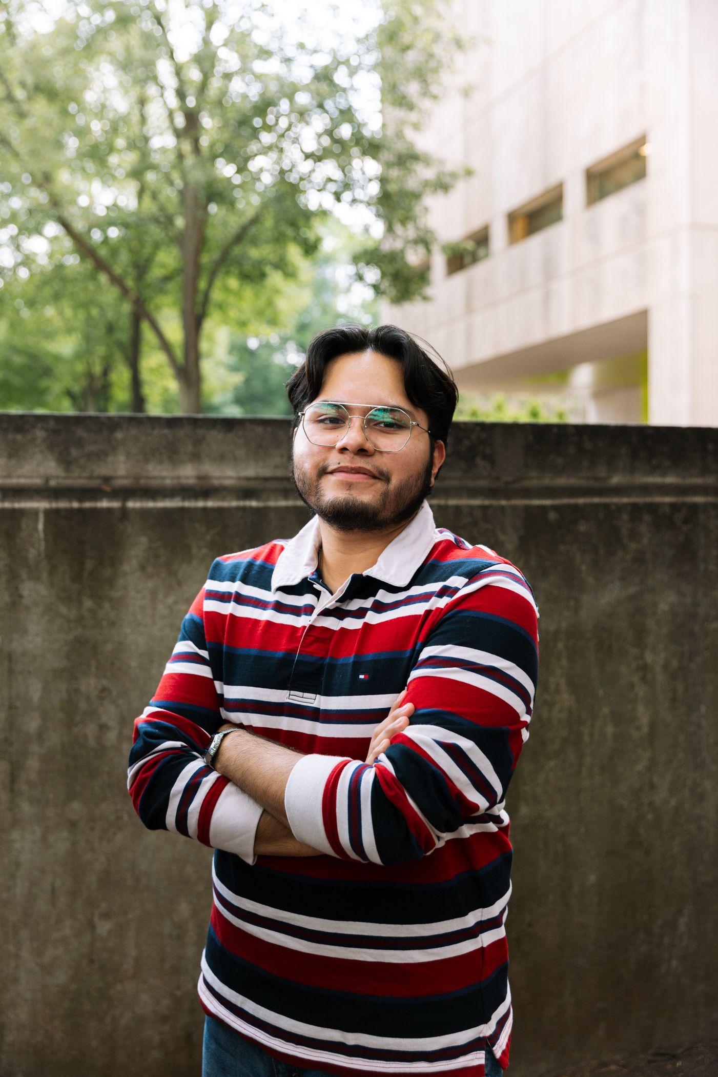 A student poses with arms crossed outside of a campus building