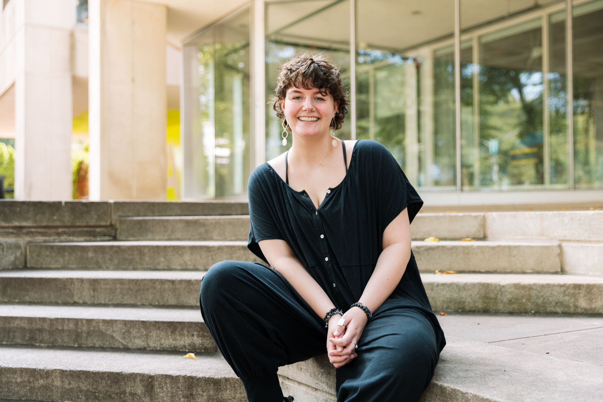 A student in all black sits on the steps of a campus building