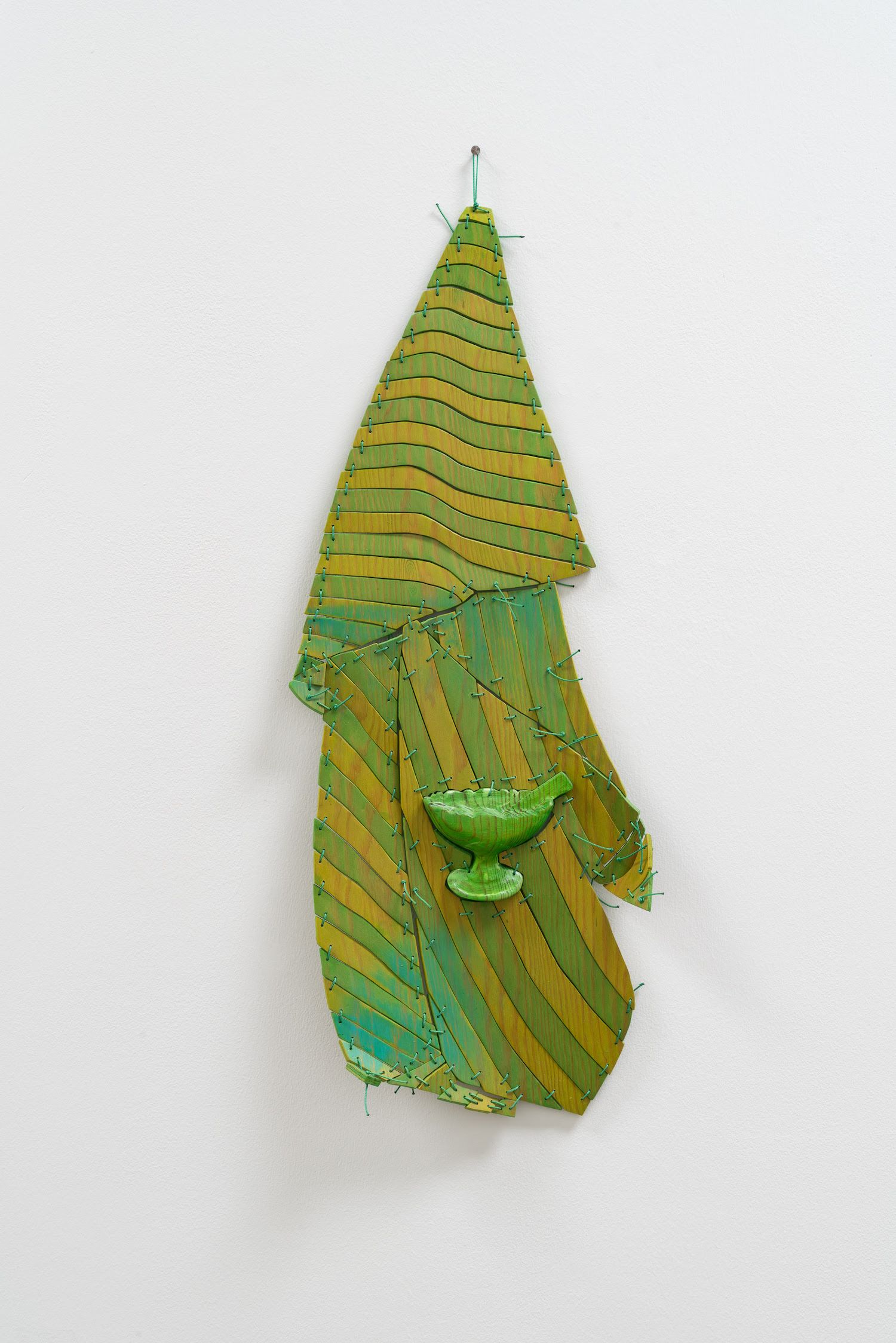 A wooden yellow and green sculpture on a white wall