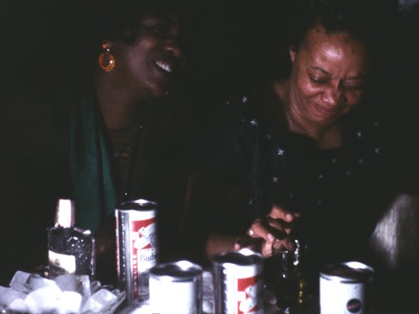 A photograph of two people laughing. In front of them are several cans on a table.