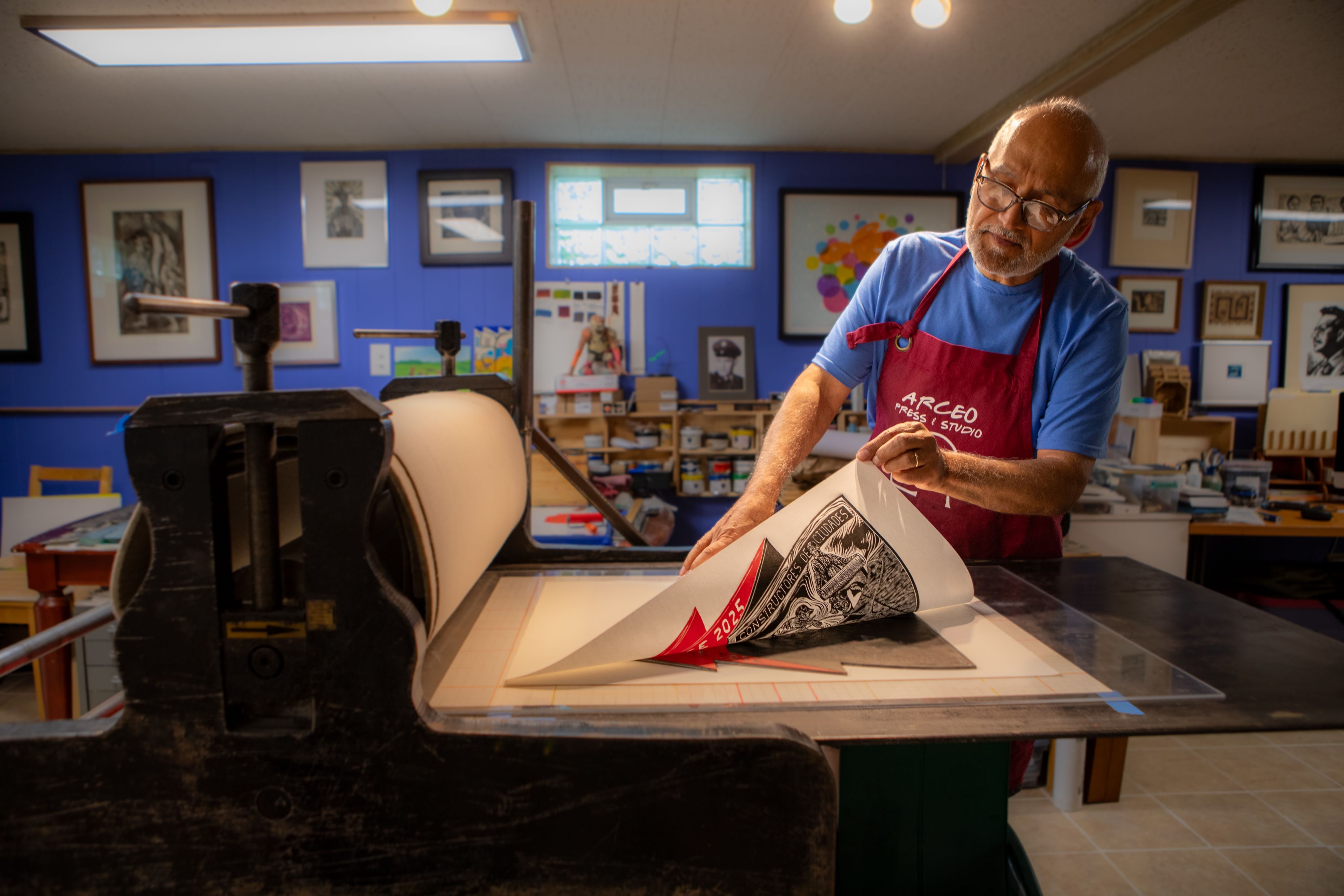 An artist pulls a print from a press in a blue room