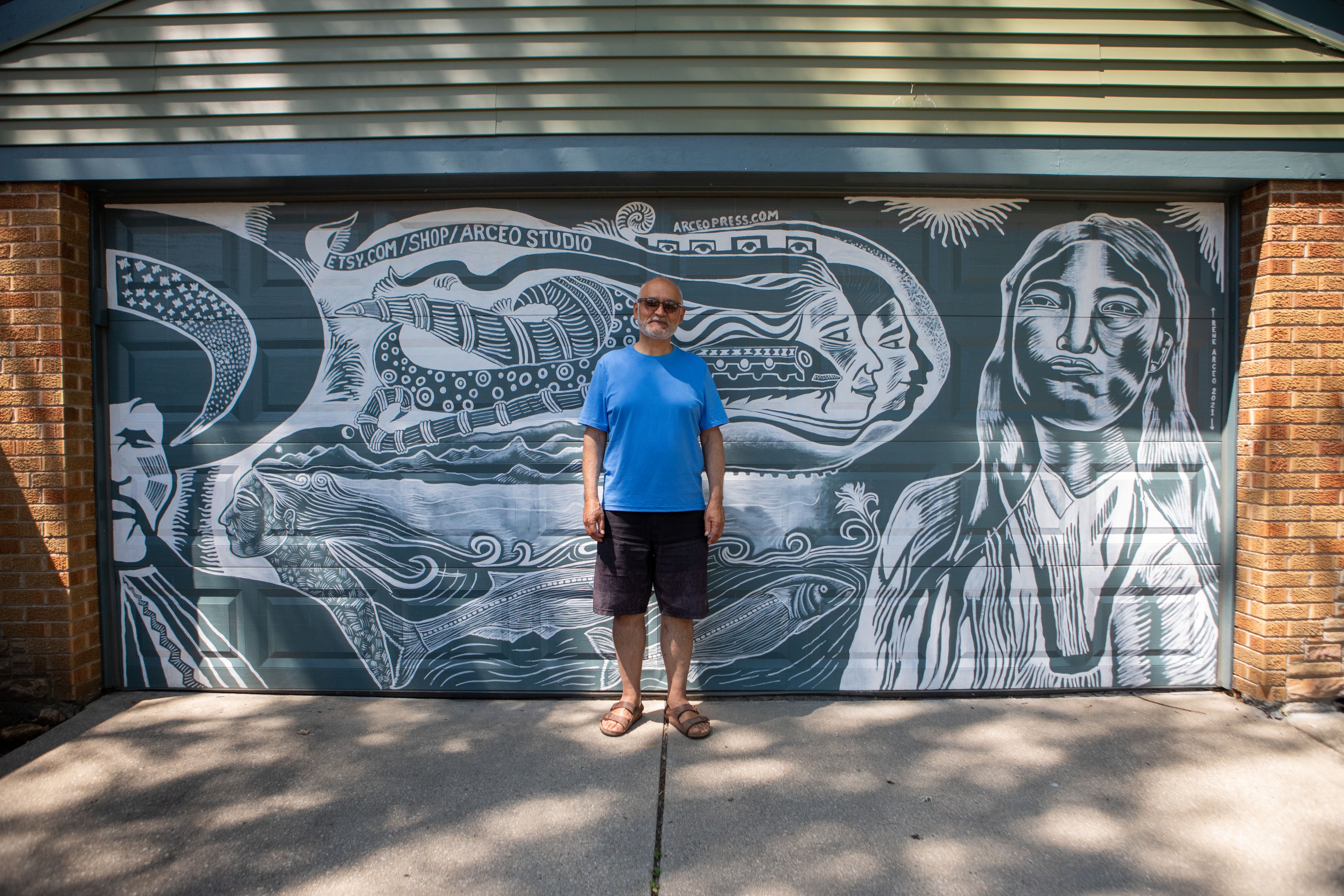 An artist in a blue shirt stands in front of a black and white mural