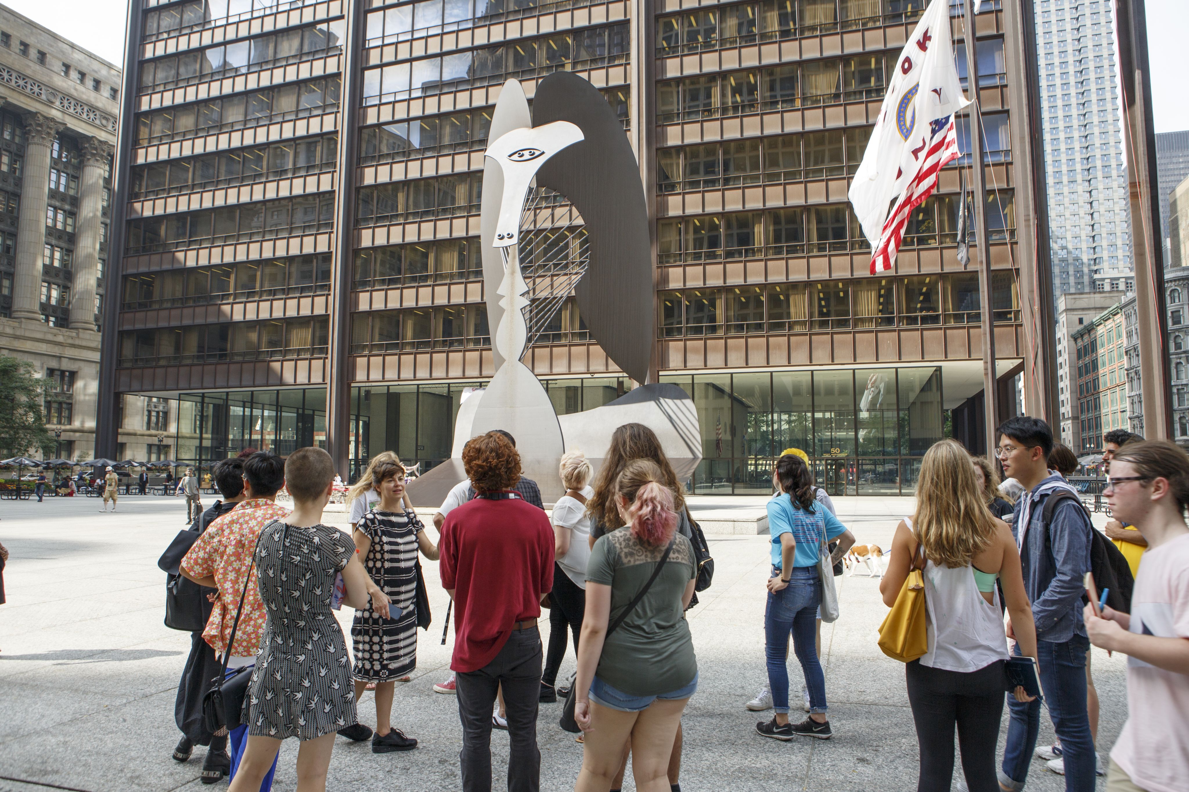 A group of student look up at a large metal sculpture in a downtown plaza