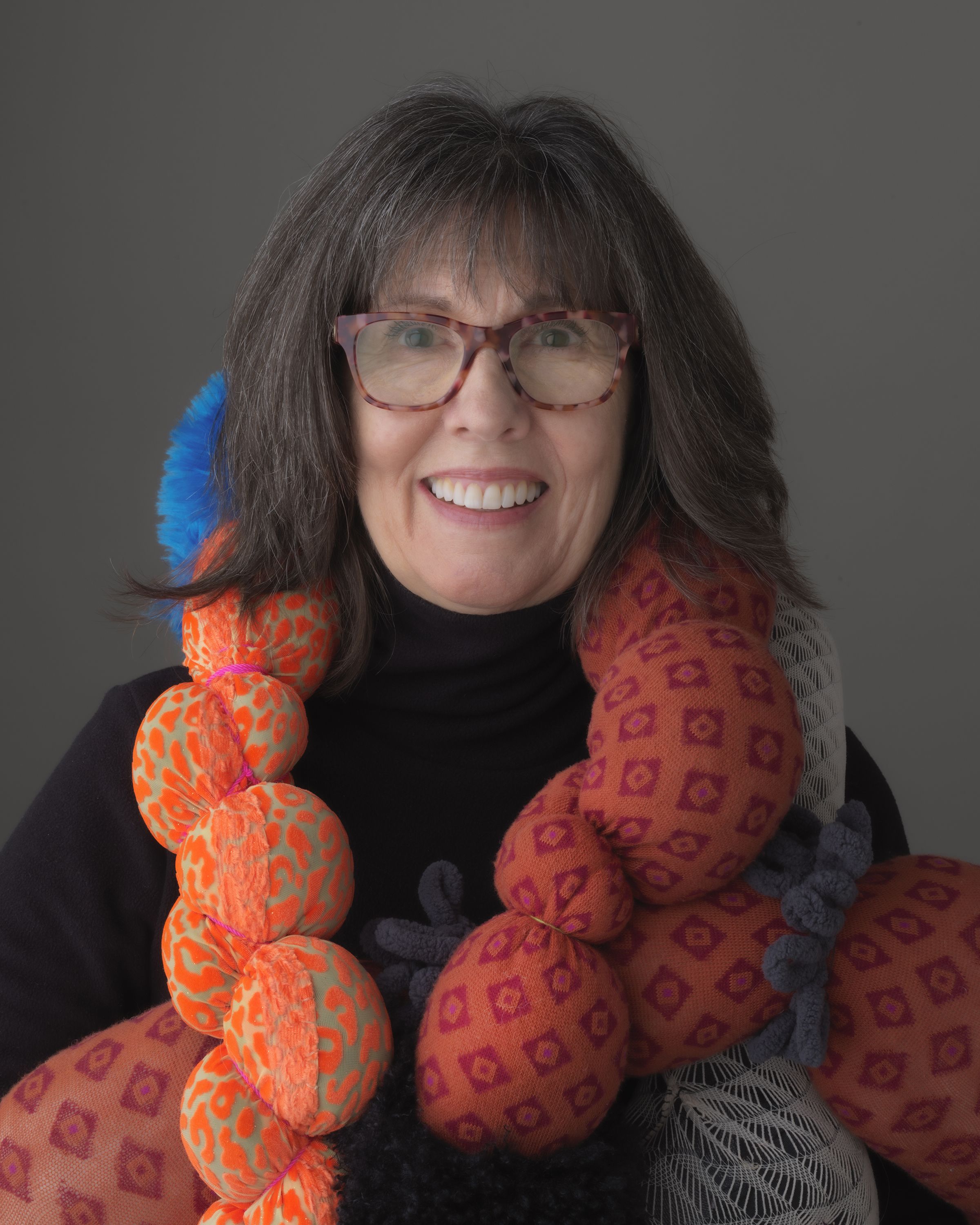 A portrait of a woman in a black turtleneck wearing fiber art