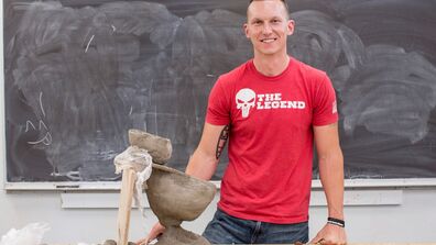 A man in a red t-shirt stands in front of a clay work table