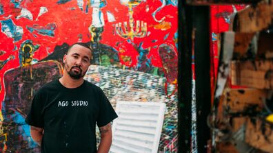The artist stands in from of a piece rendered in the style of a graffiti 
