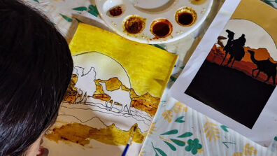 A young girl painting a desert landscape with spices on a table, focused and creative