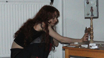 A woman with long brown hair crouching over a coffee table making art. 