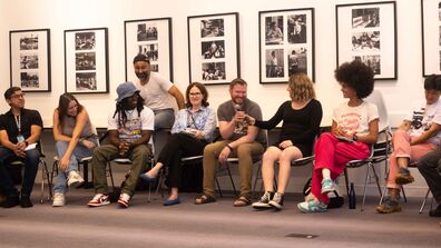 A photo of students sitting in chairs passing around a microphone