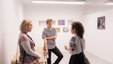 A photo of three people standing in front of some art in a white room