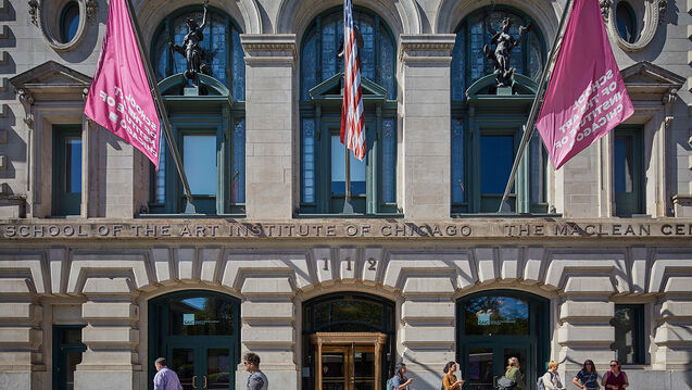 A majestic building in downtown Chiciago with three flags.