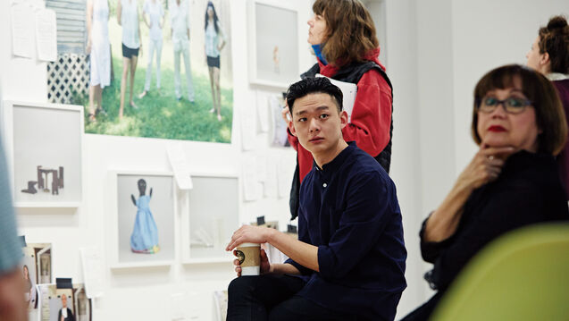 Two students in front of a wall of hanging art pieces.