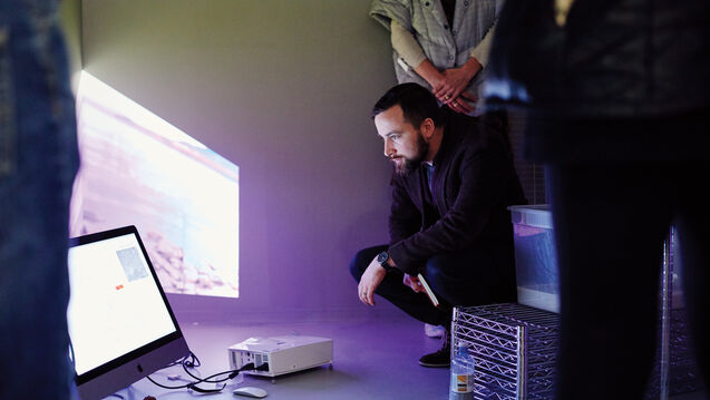 A person crouching down to look at a monitor on the floor. 