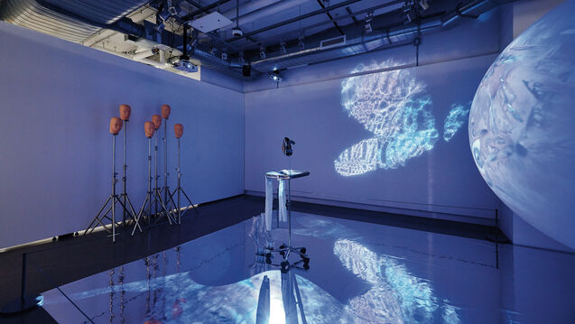 A mirror on the floor with a metal object in the center with a set of mannequin heads on tripods placed along the wall. 